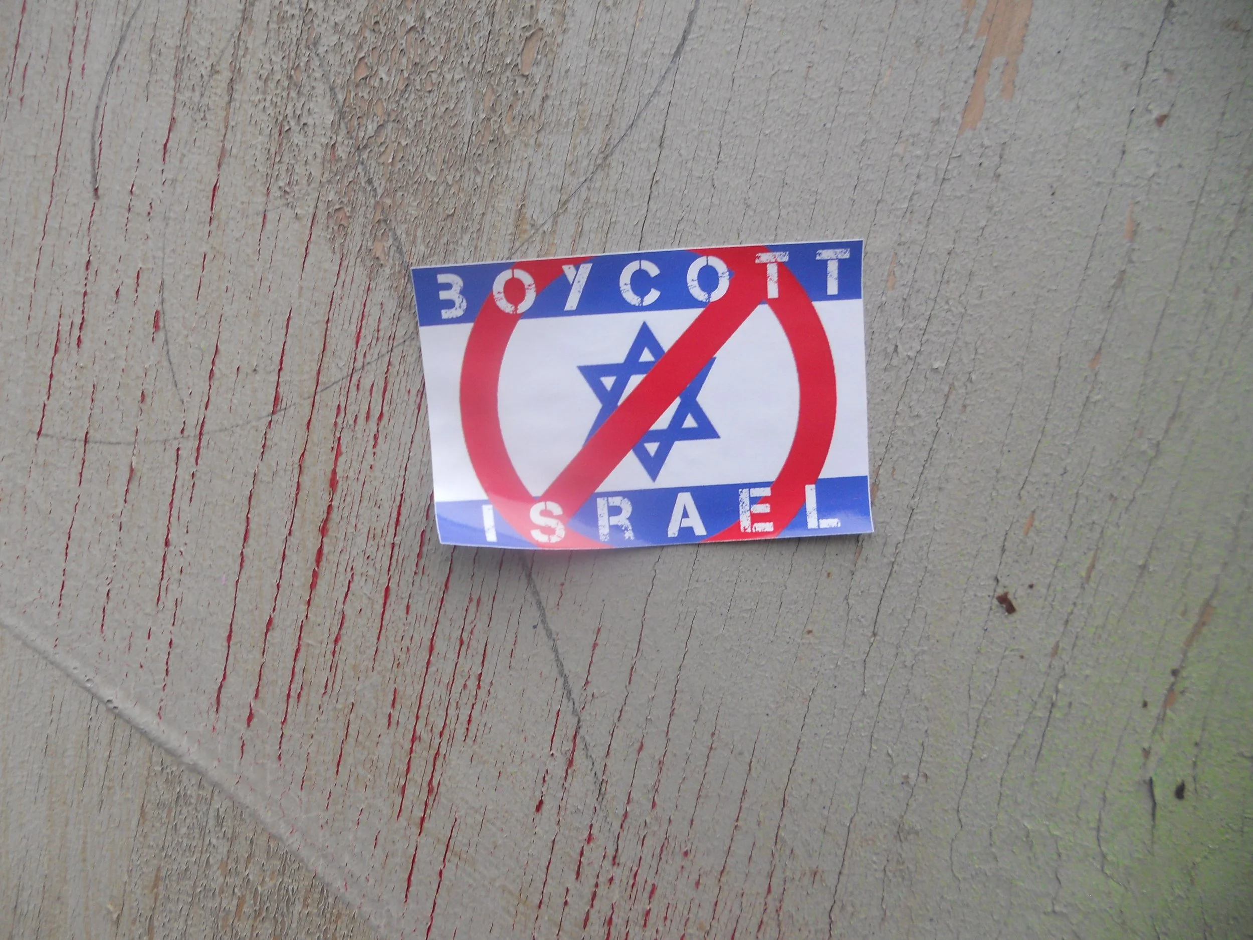 Christopher Clucas -  with the text 'BOYCOTT ISRAEL' and a blue Star of David crossed out, on a wooden surface.