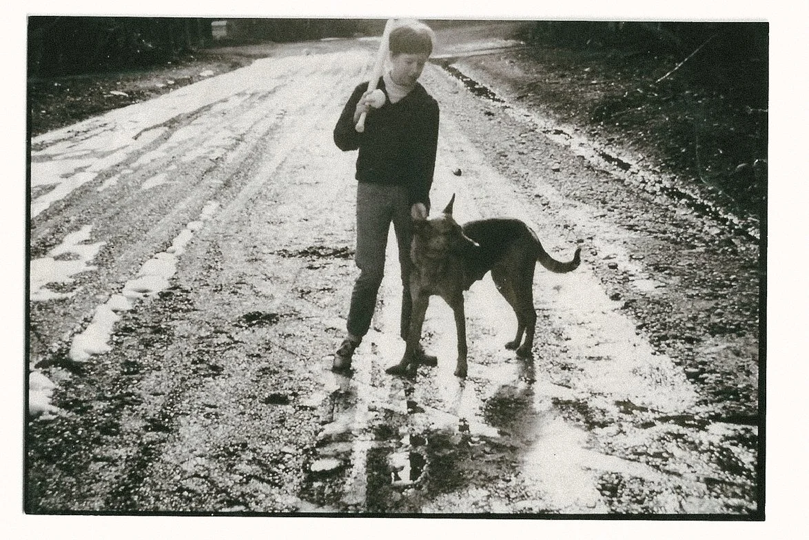 A boy standing on a wet, muddy road holding a leash attached to a large German Shepherd dog.