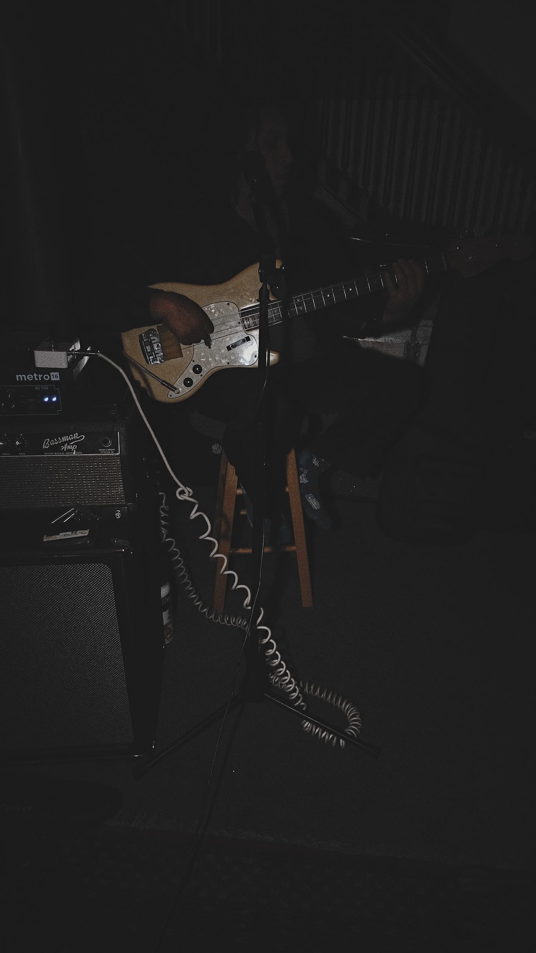 A person playing an electric guitar in a dark room with musical equipment around.