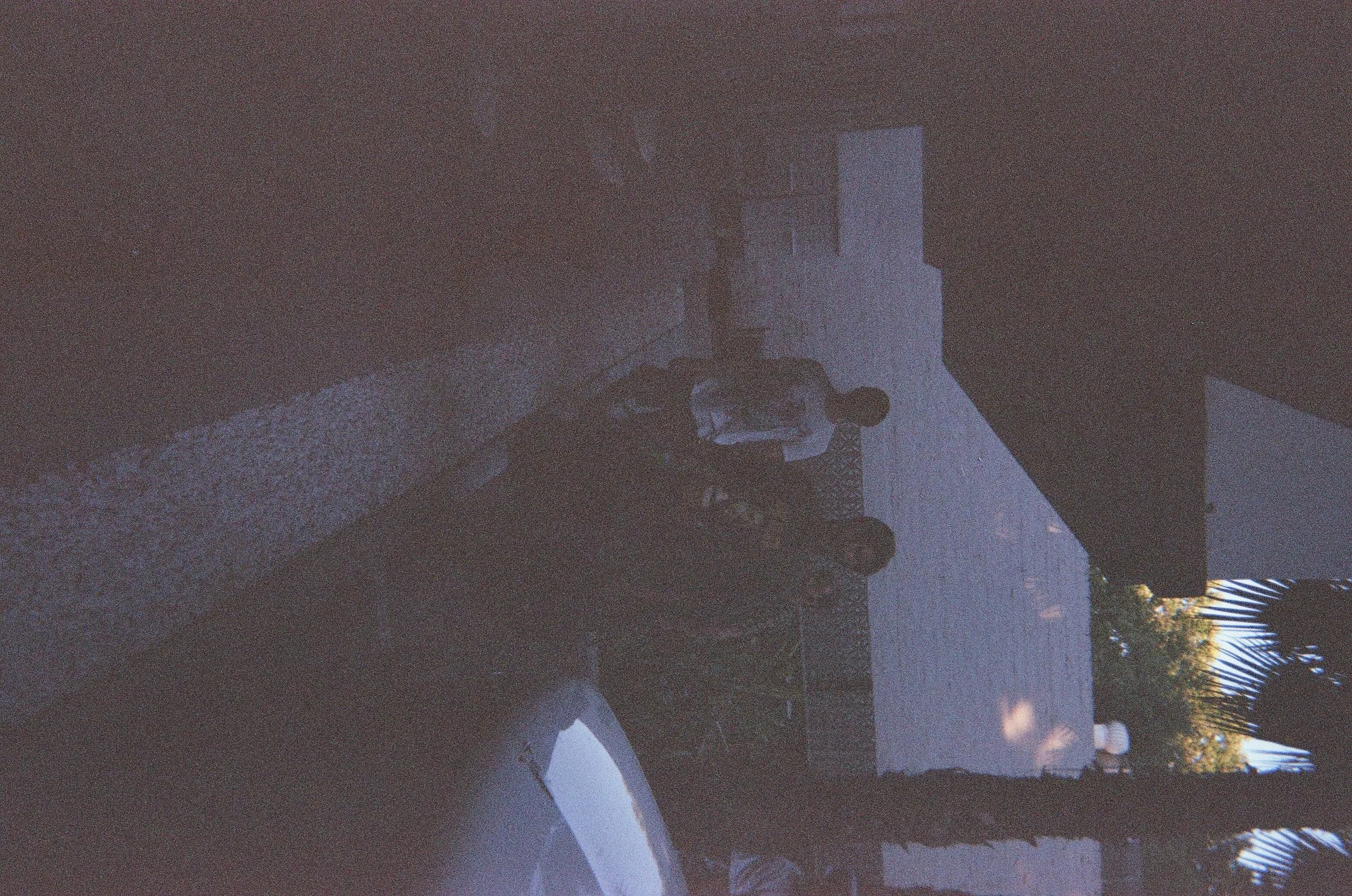 A group of people standing outside near a brick wall and a building with trees and moon in the background during dusk.