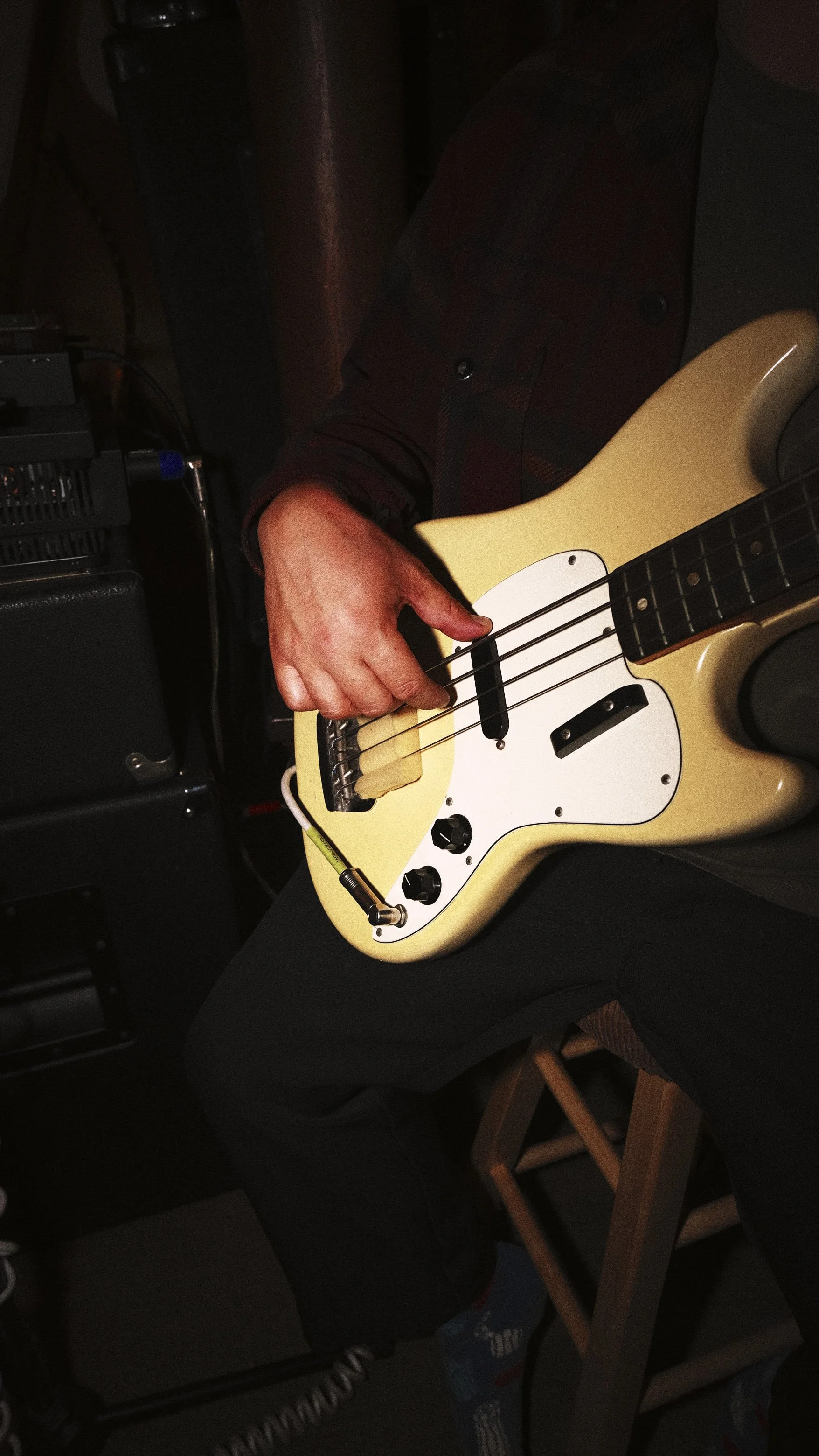 Person sitting on a chair playing a cream-colored electric bass guitar.