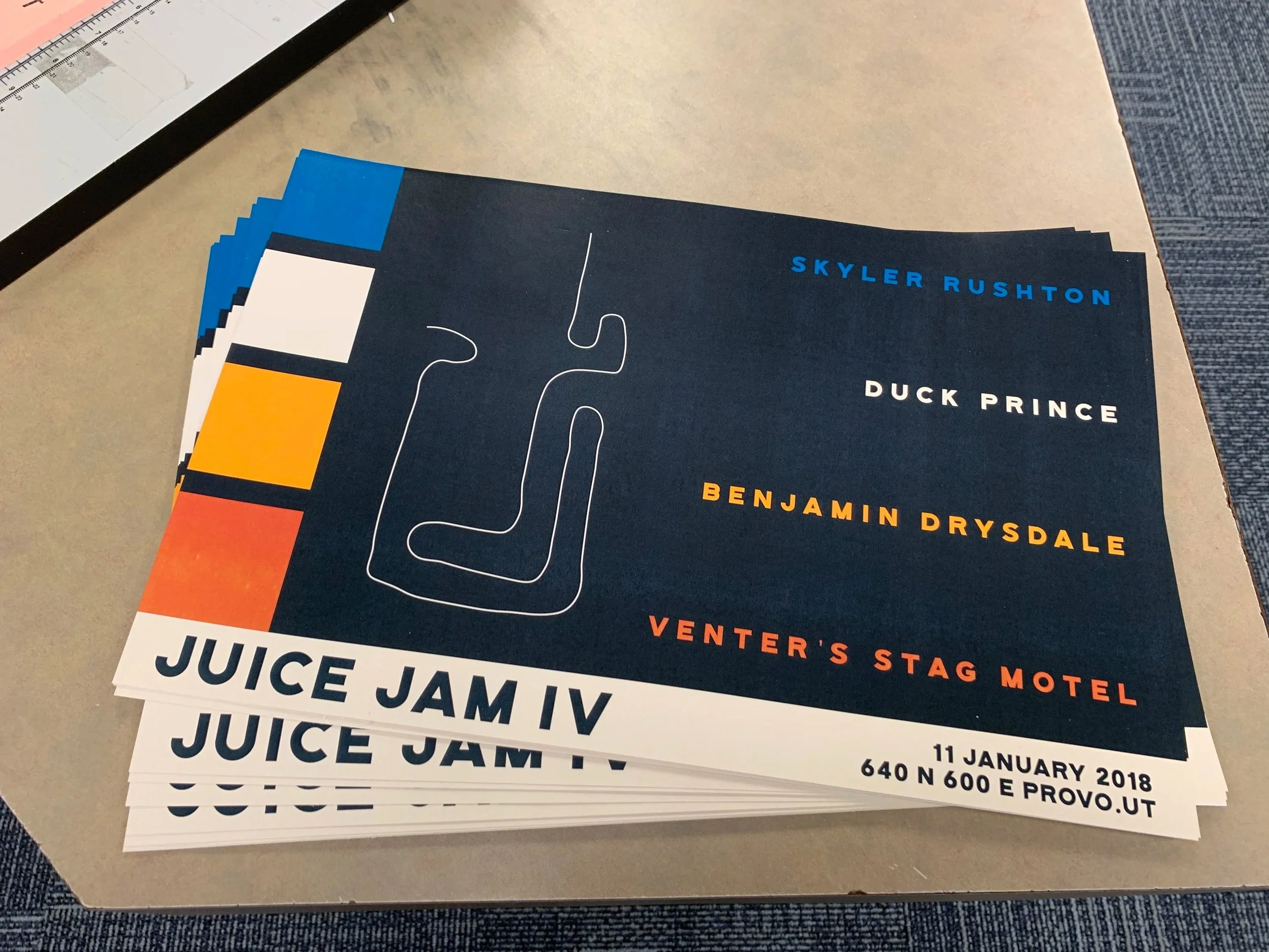 Stack of concert or event flyers on a table, featuring a dark blue background with colorful blocks, a white line drawing of a vinyl record, and text listing performers Skyler Rushton, Duck Prince, Benjamin Drysdale, and Venter's Stag Motel, plus even