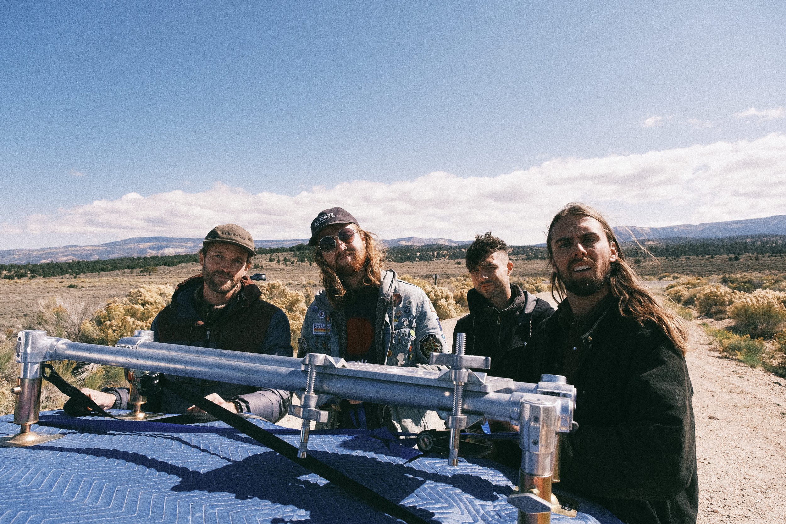 Four men standing outdoors in a desert landscape under a partly cloudy sky.
