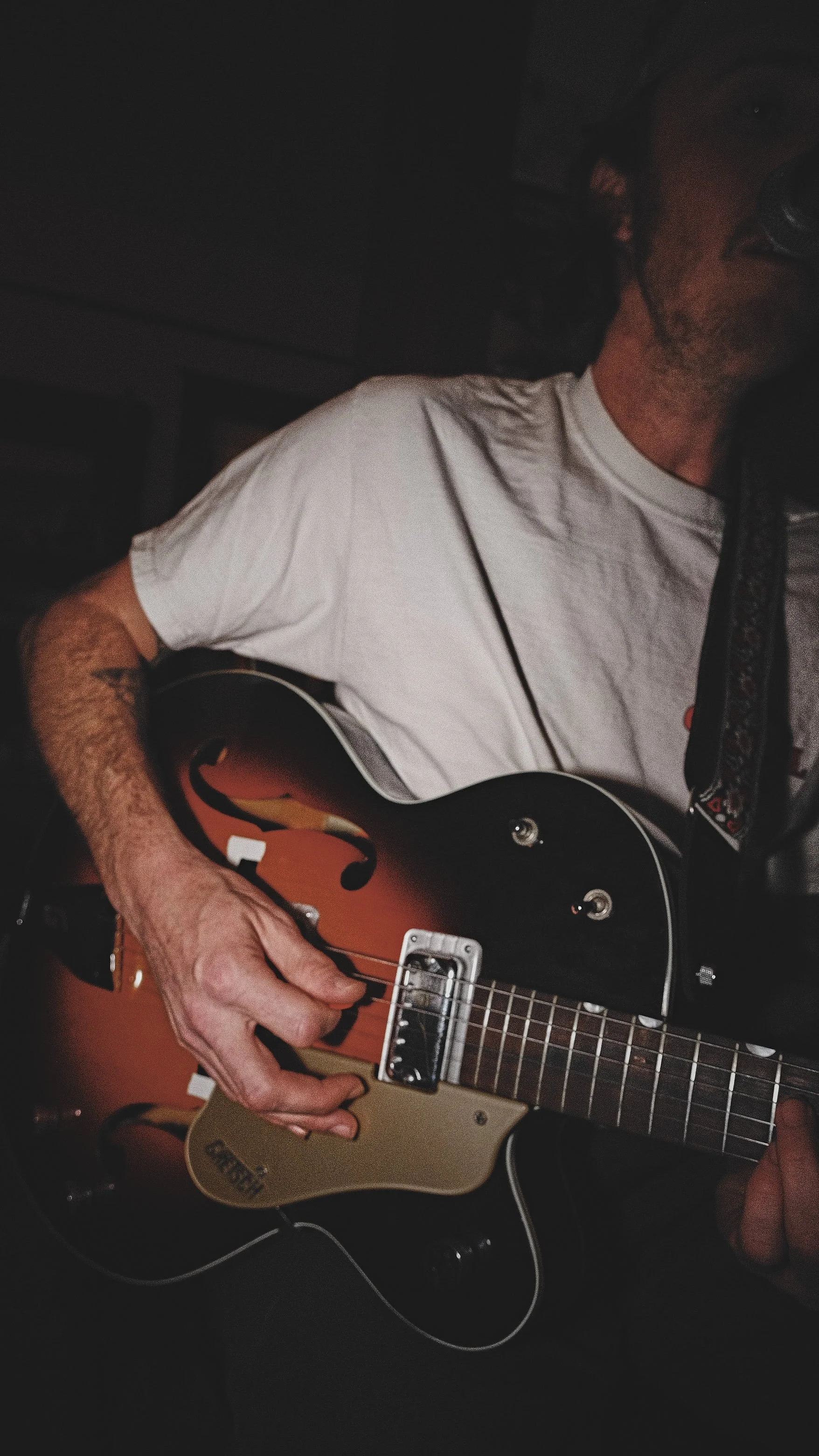 Person playing an orange and black electric guitar with a sunburst finish in a dark room.