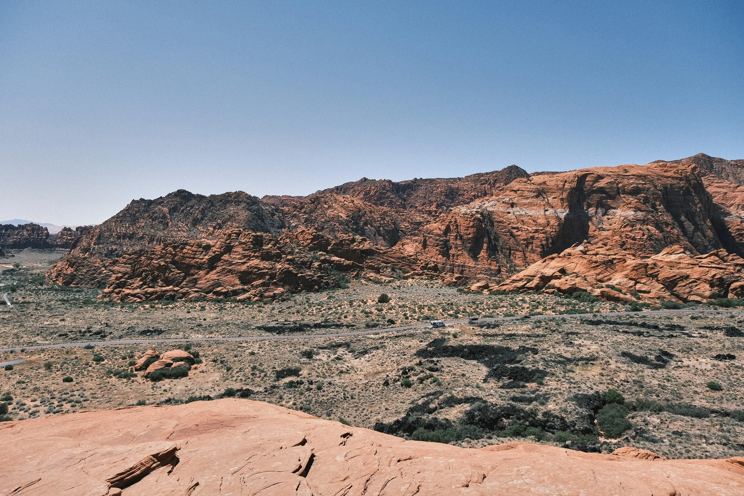 Desert landscape with red rock formations, sparse vegetation, and clear blue sky.