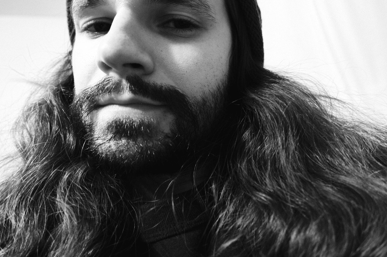Close-up black and white portrait of a man with long hair and a beard.