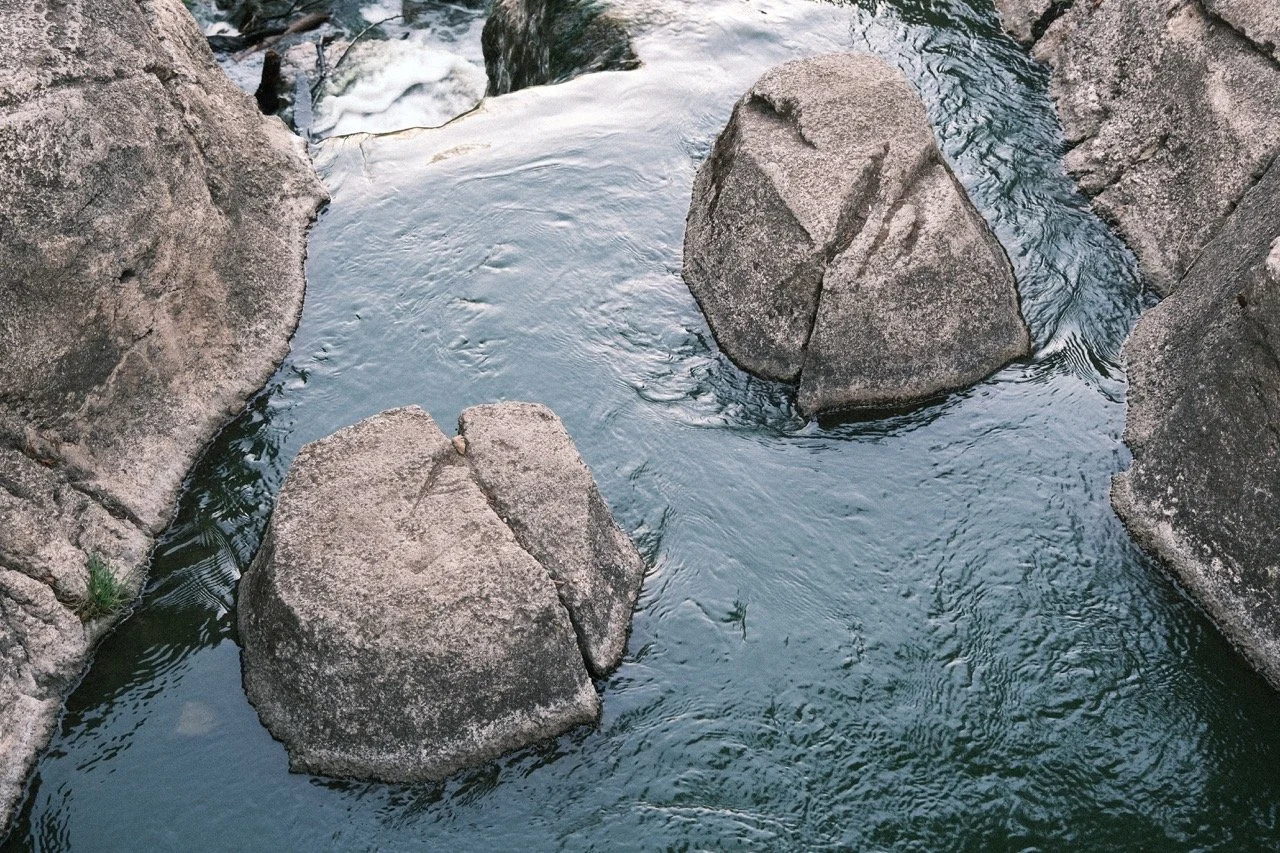 A small stream flowing around large rocks in a natural outdoor setting.