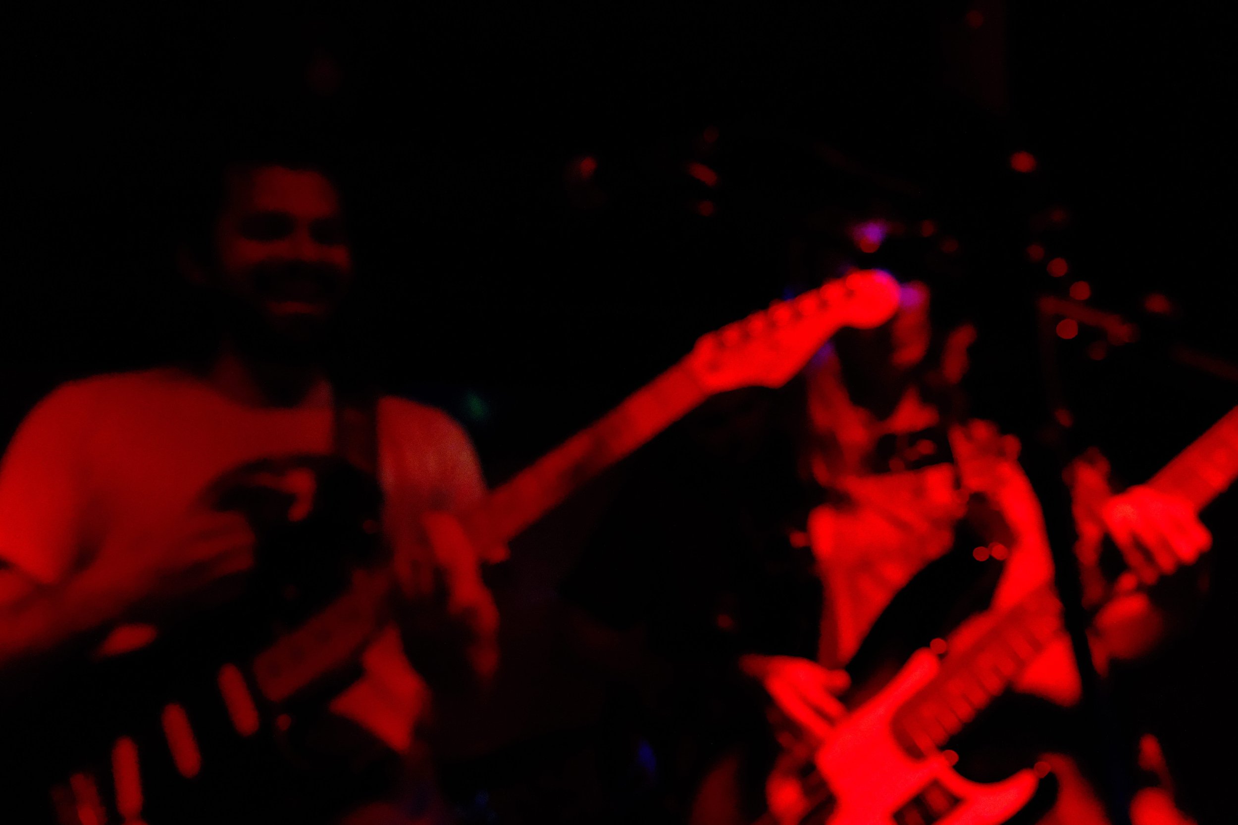 Two musicians playing guitars on a dark stage illuminated by red lights.