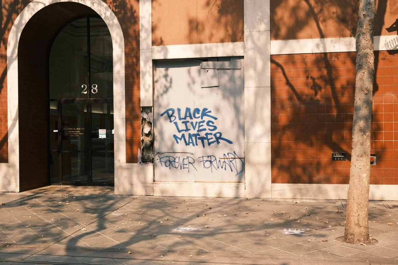 Graffiti on a white panel attached to a brick building, with the words "Black Lives Matter" in blue spray paint and "Forever Forward