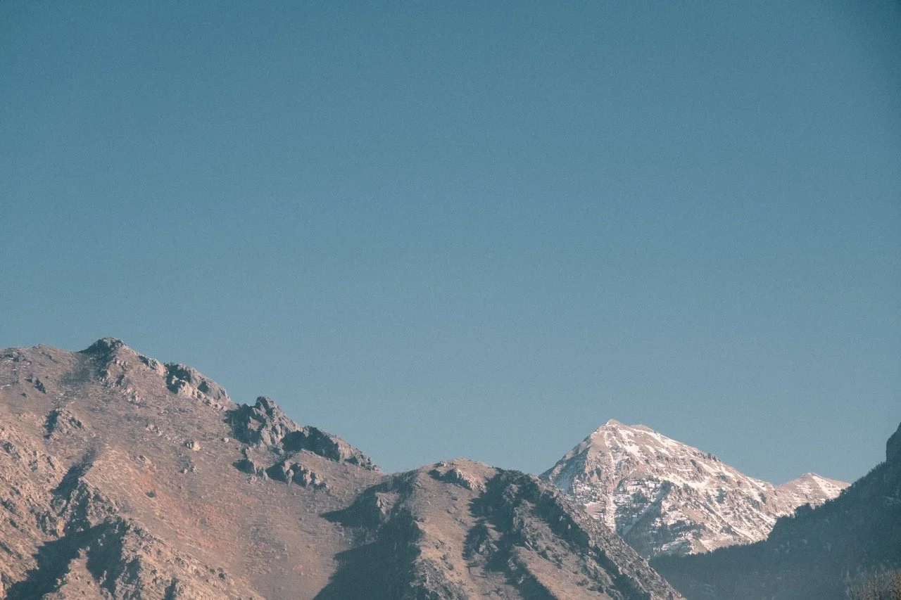 Mountain range with rocky peaks and some snow on the highest peaks under a clear blue sky.