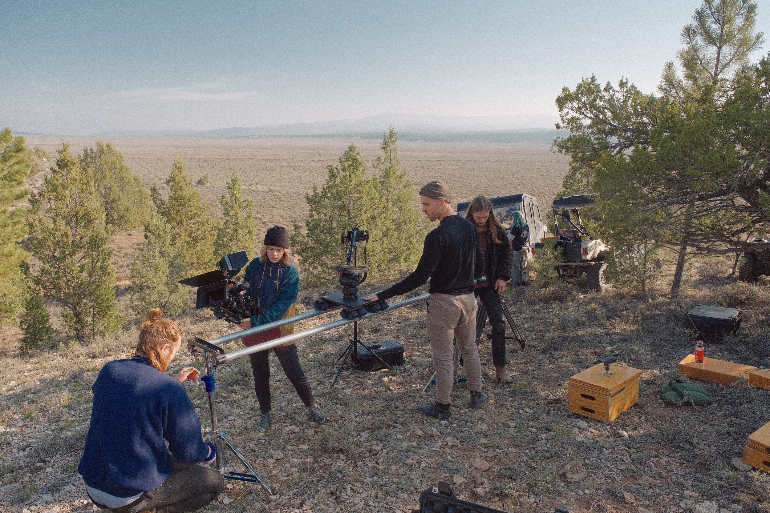 Filmmakers filming outdoors in a remote, open landscape with trees, using professional camera equipment.