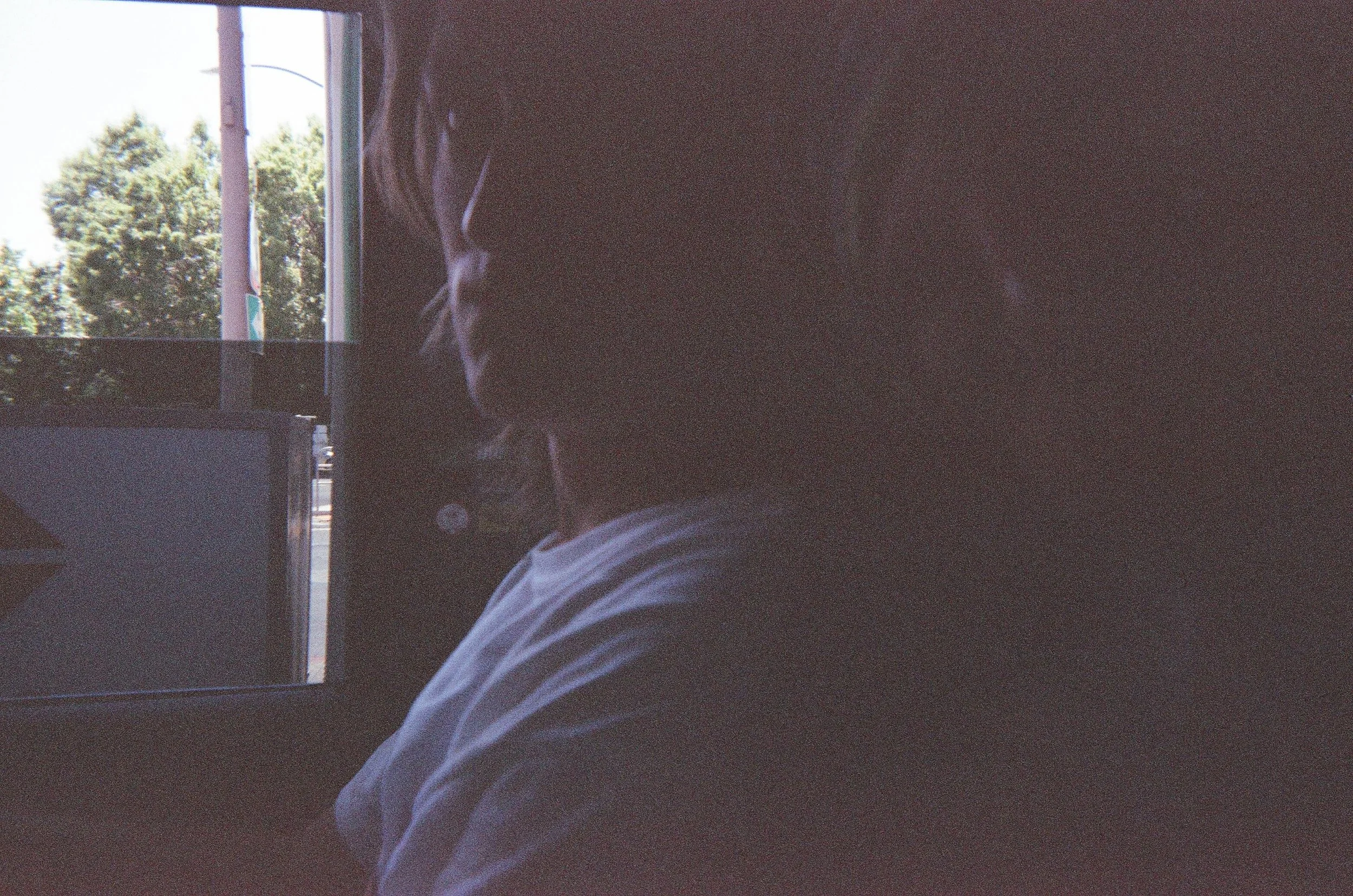 Person sitting indoors with a window behind them, partially turned to the side, wearing glasses and a white shirt.