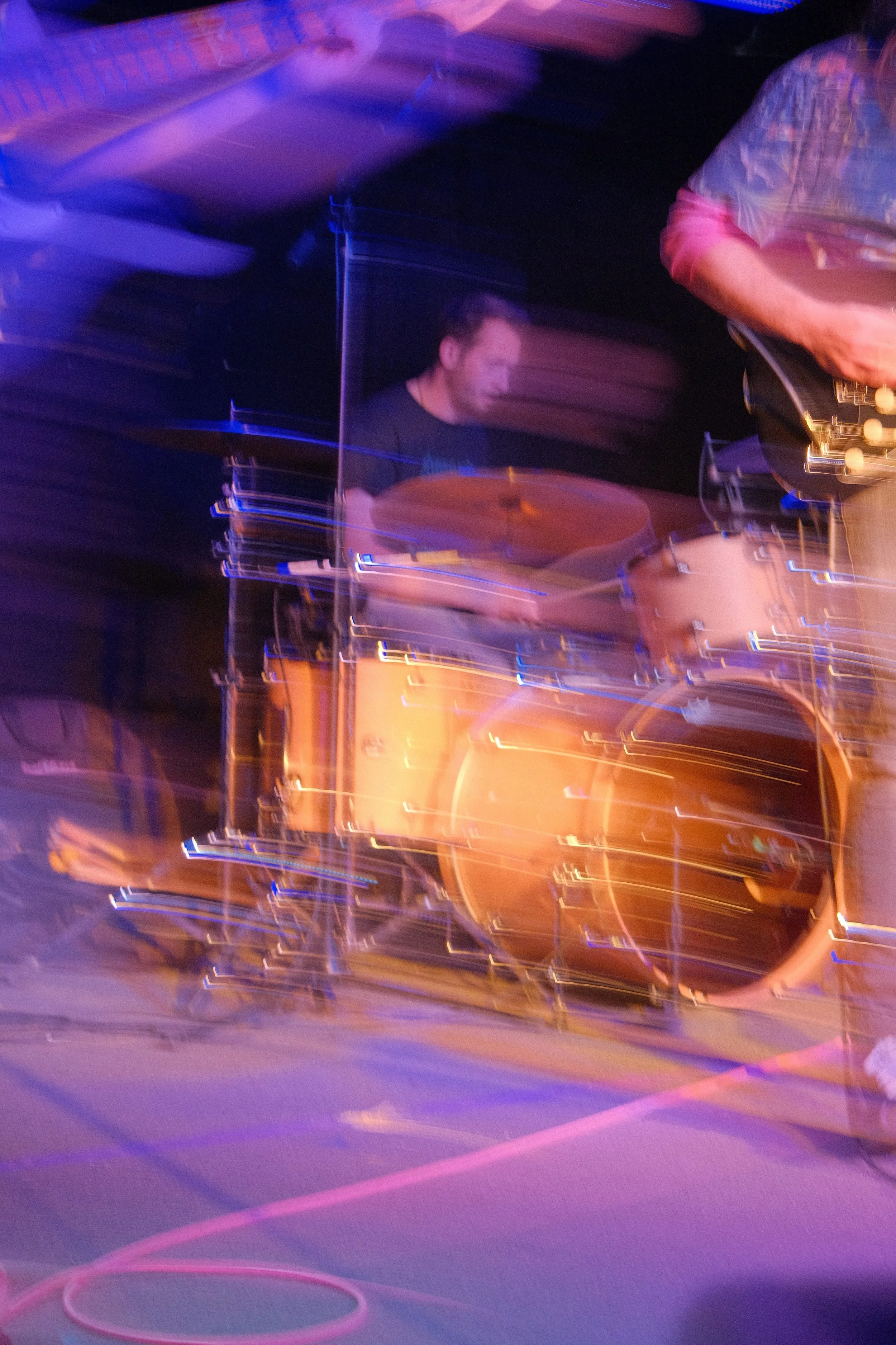A musician playing drums on stage, captured with motion blur and colored stage lighting.