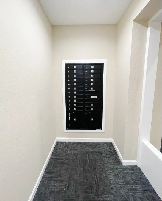 A black electrical breaker panel mounted on the wall in a small, beige-colored room with gray carpet flooring.