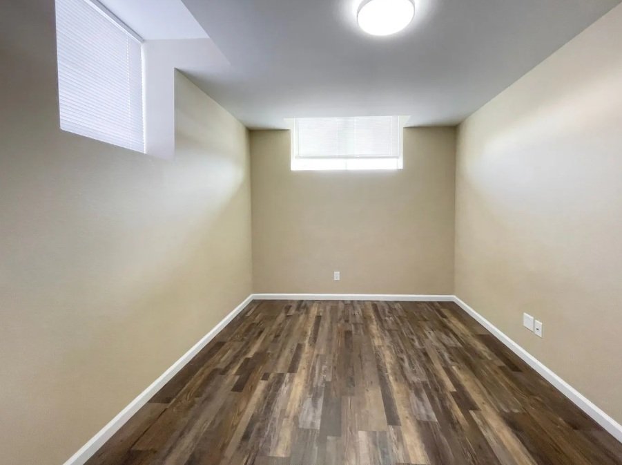 Empty room with beige walls, hardwood floors, and two small windows near the ceiling, with a ceiling light fixture.