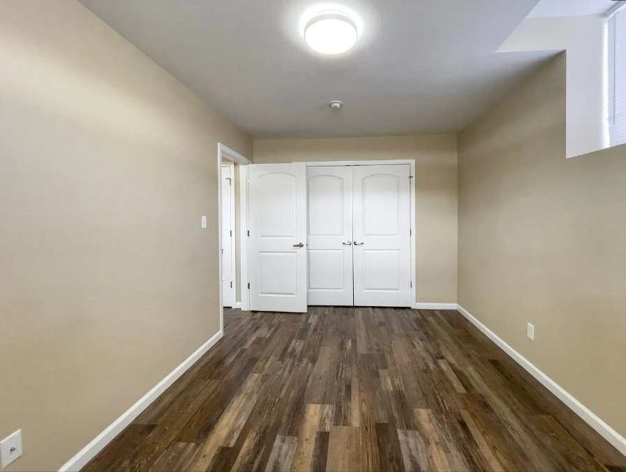 Empty room with beige walls, wooden floor, white closet doors, and a ceiling light fixture.