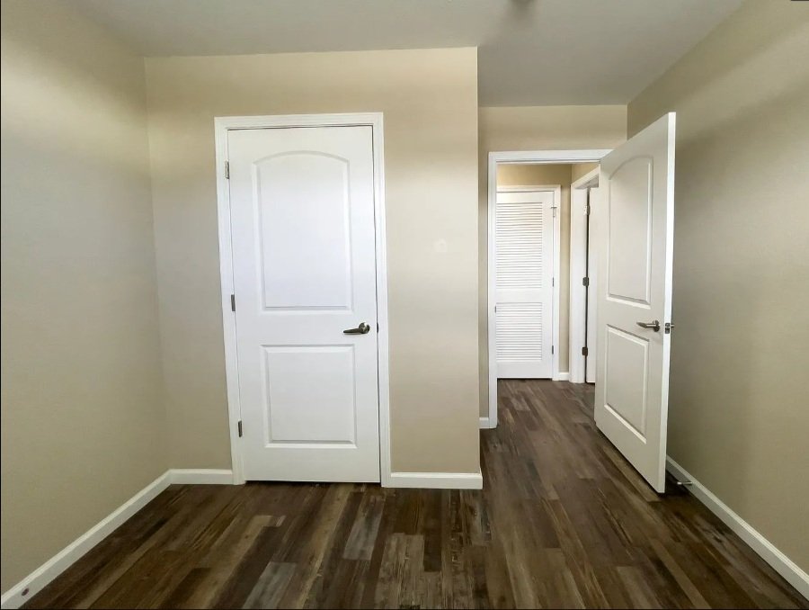 Empty room with beige walls, white doors, and dark wood flooring.