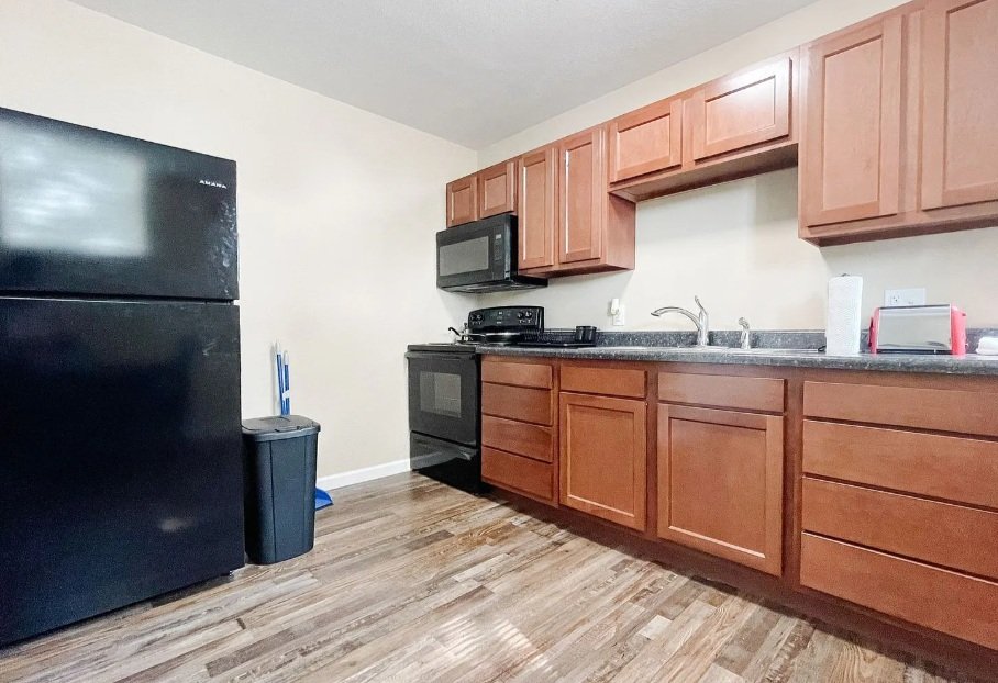 Kitchen with black refrigerator, trash can, wooden cabinets, black stove, microwave, and countertop with paper towel roll and toaster.
