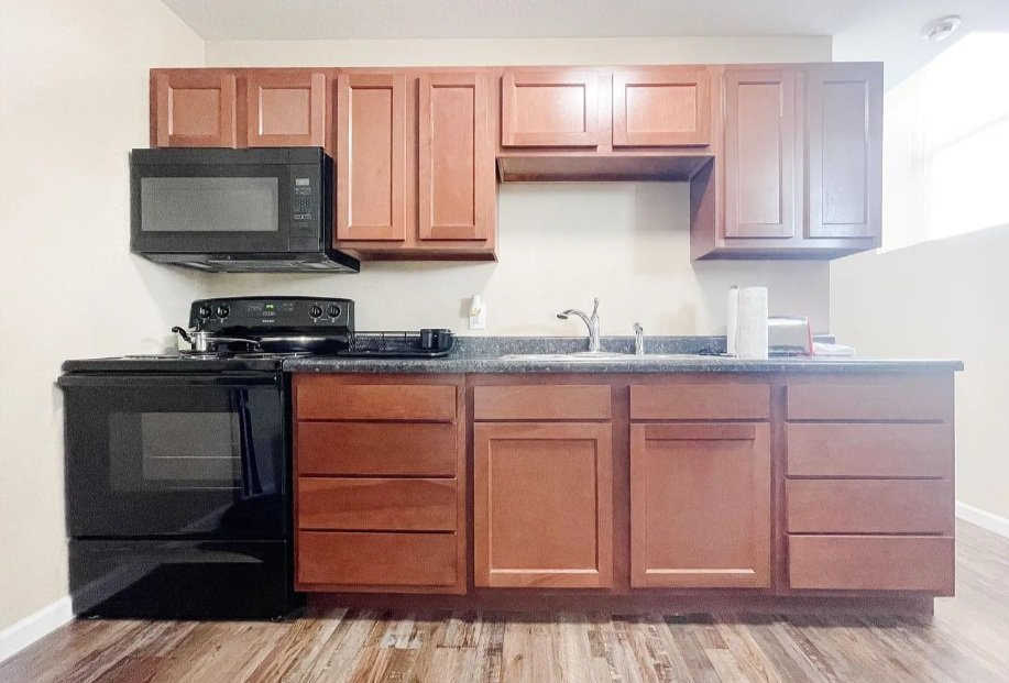 Kitchen with black appliances, wooden cabinets, a countertop, a microwave, an oven, a sink, and a paper towel roll.