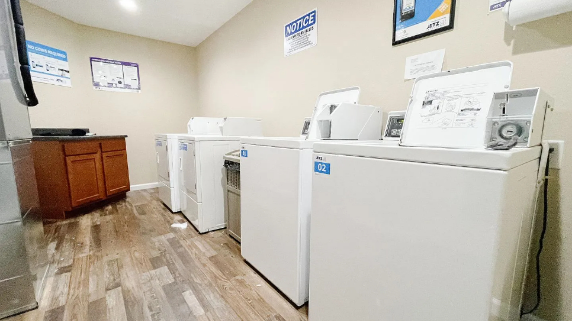 A laundry room with four white top-loading washing machines and a brown wooden cabinet against a beige wall.