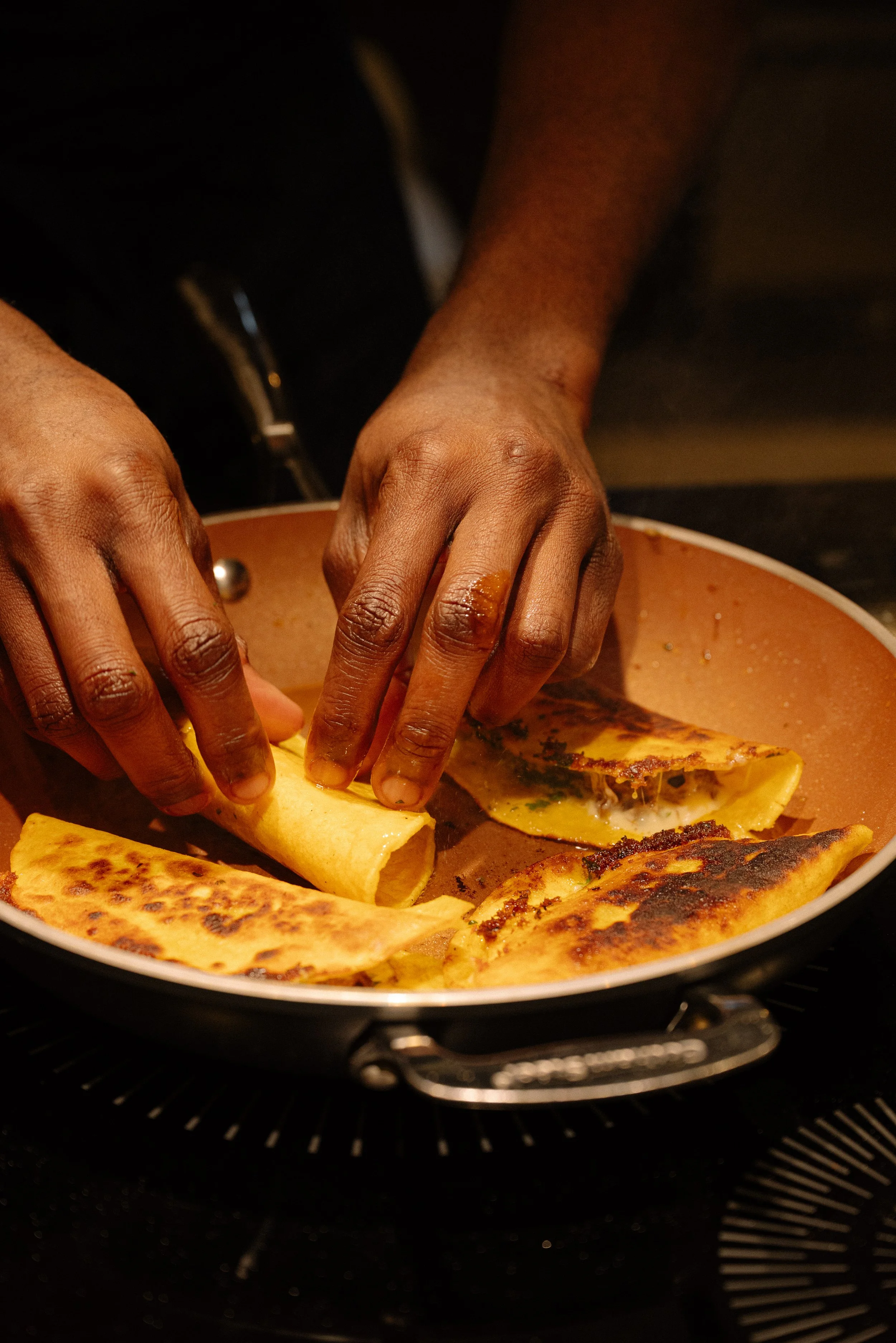 Hands cooking cheese quesadillas in a black skillet on a stovetop.
