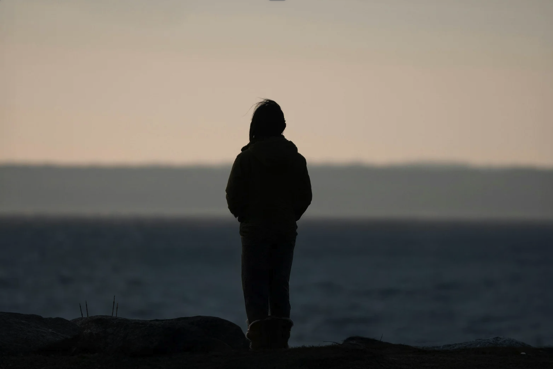 Silhouette of a person standing by the water at sunset, representing anxious attachment, reflection, and emotional processing