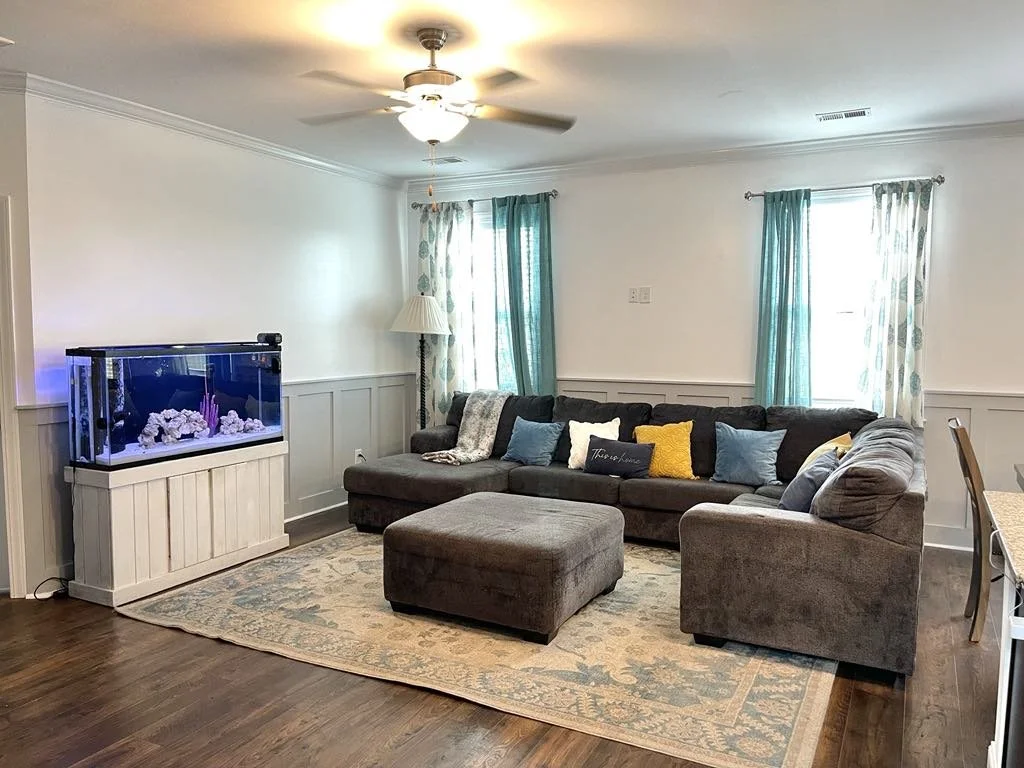 Living room with a sectional sofa, ottoman, aquarium, and window curtains.