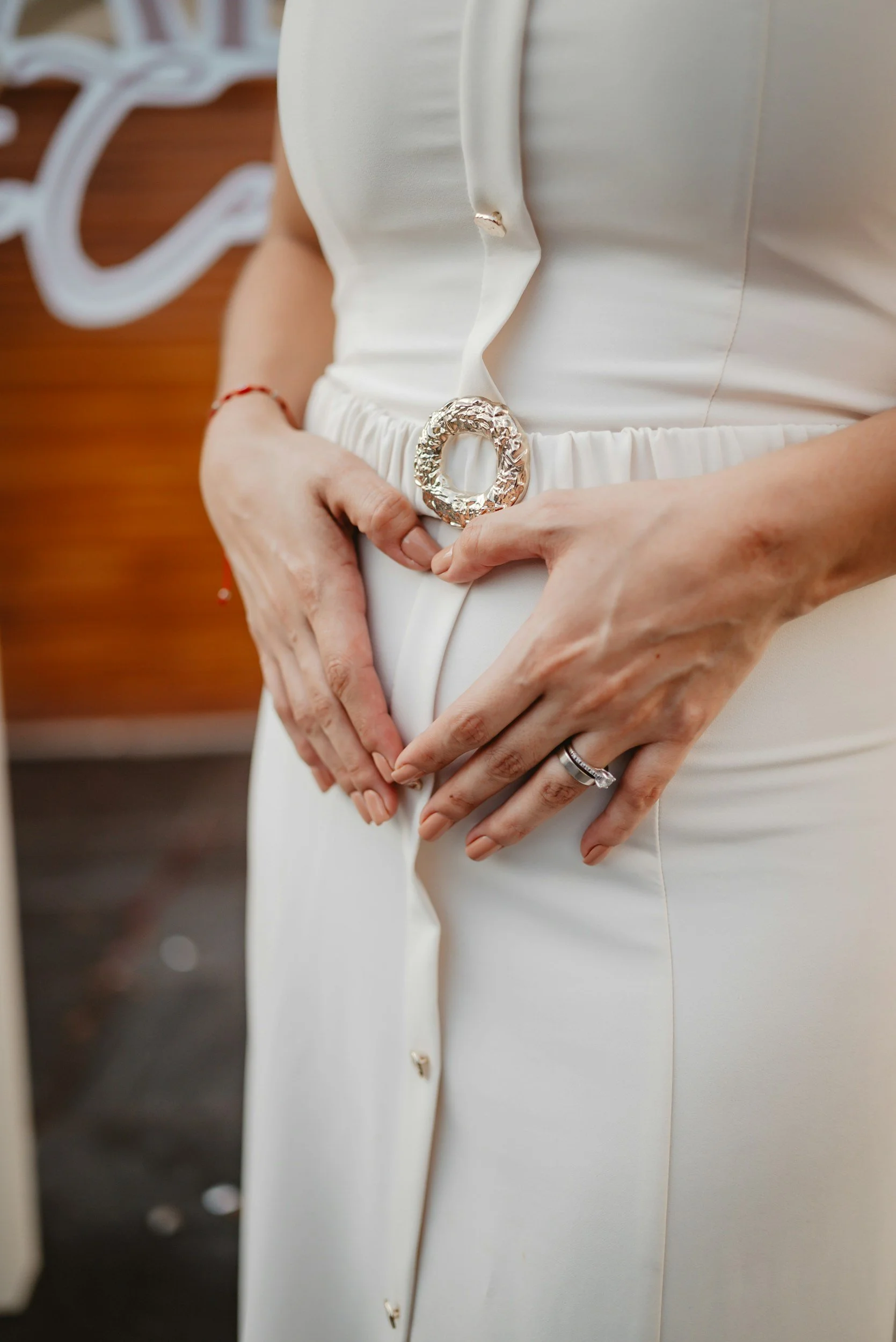 Person wearing a white dress with a fabric belt and large decorative silver belt buckle, hands resting on their waist with rings on their fingers.
