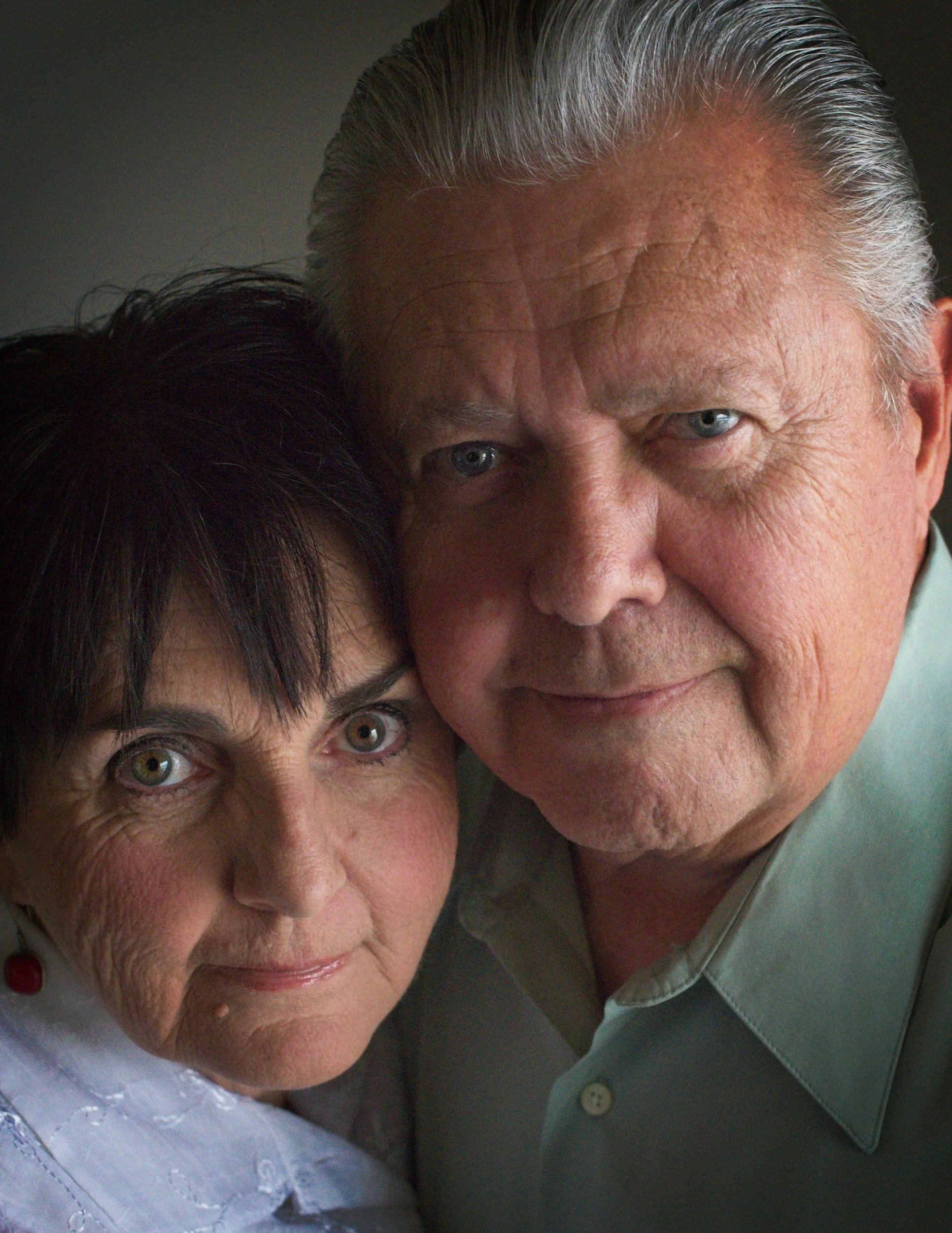 Close-up of two older adults, a woman with dark hair and a man with gray hair, close to each other, showing part of their faces including eyes, noses, and part of their mouths.
