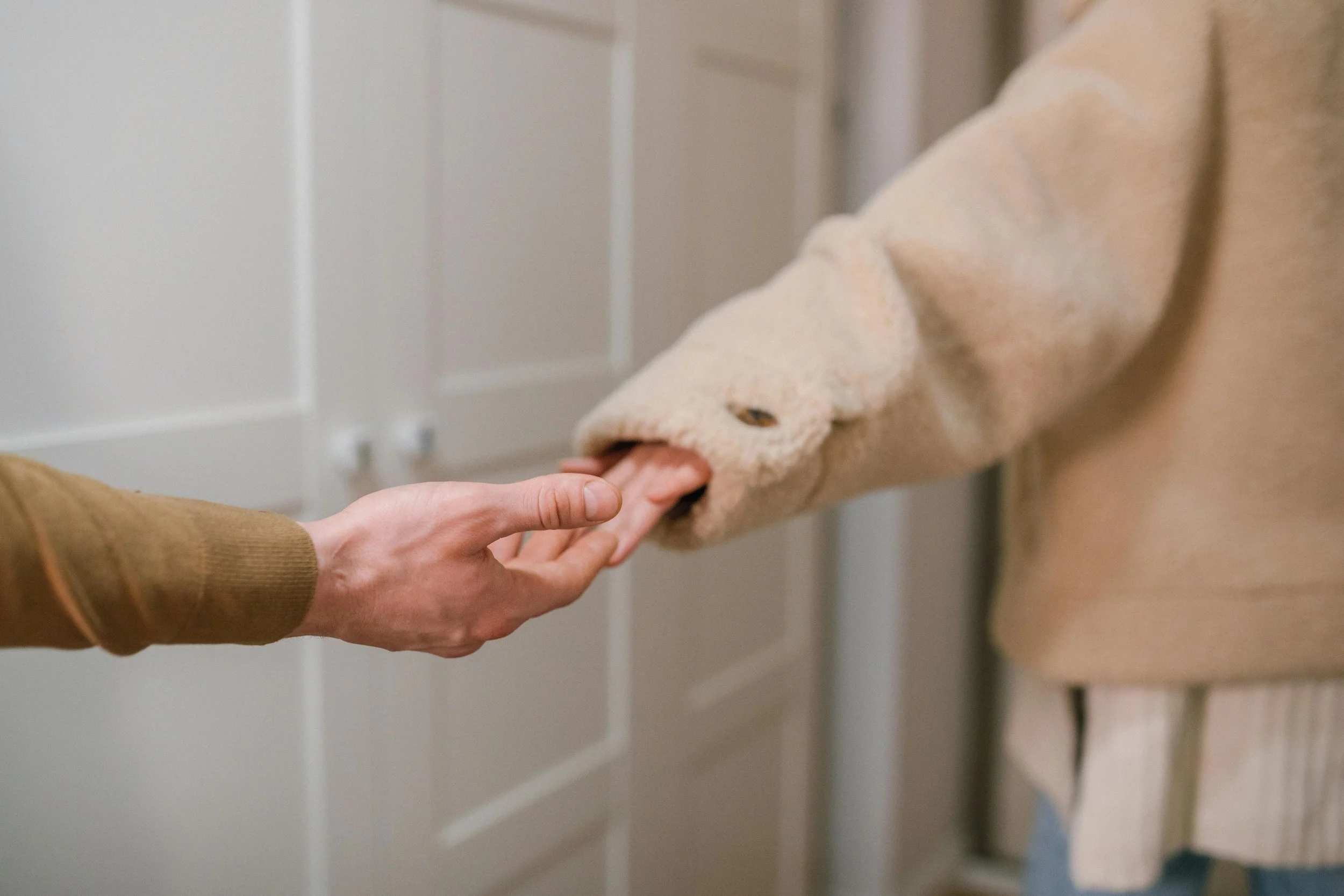 Person in a beige sweater receiving a handshake from a person in a beige coat with a fuzzy sleeve.