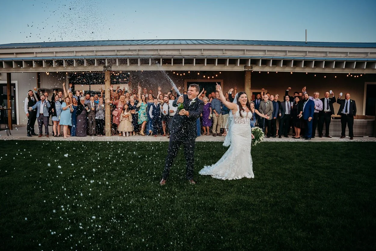 couple popping champagne with their guests at a northern michigan wedding reception