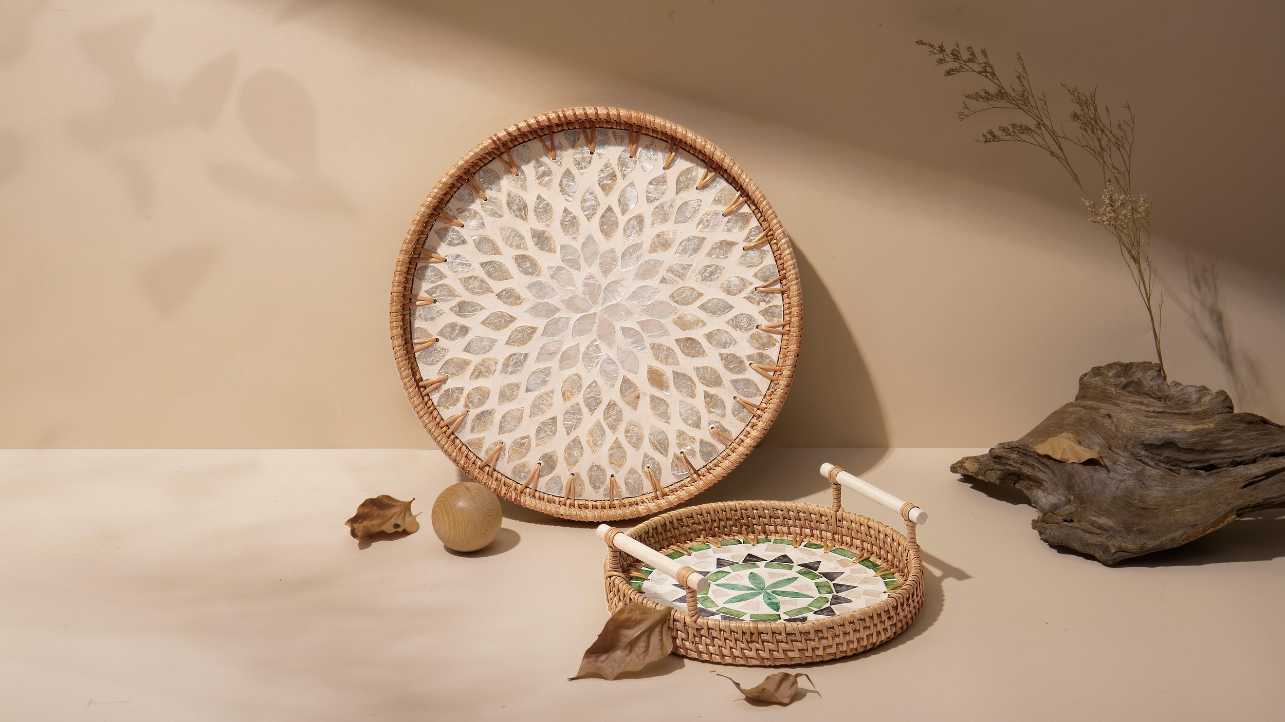 Decorative woven baskets with tile patterns, a driftwood piece, dried leaves, and a wooden ball arranged on a light-colored surface.