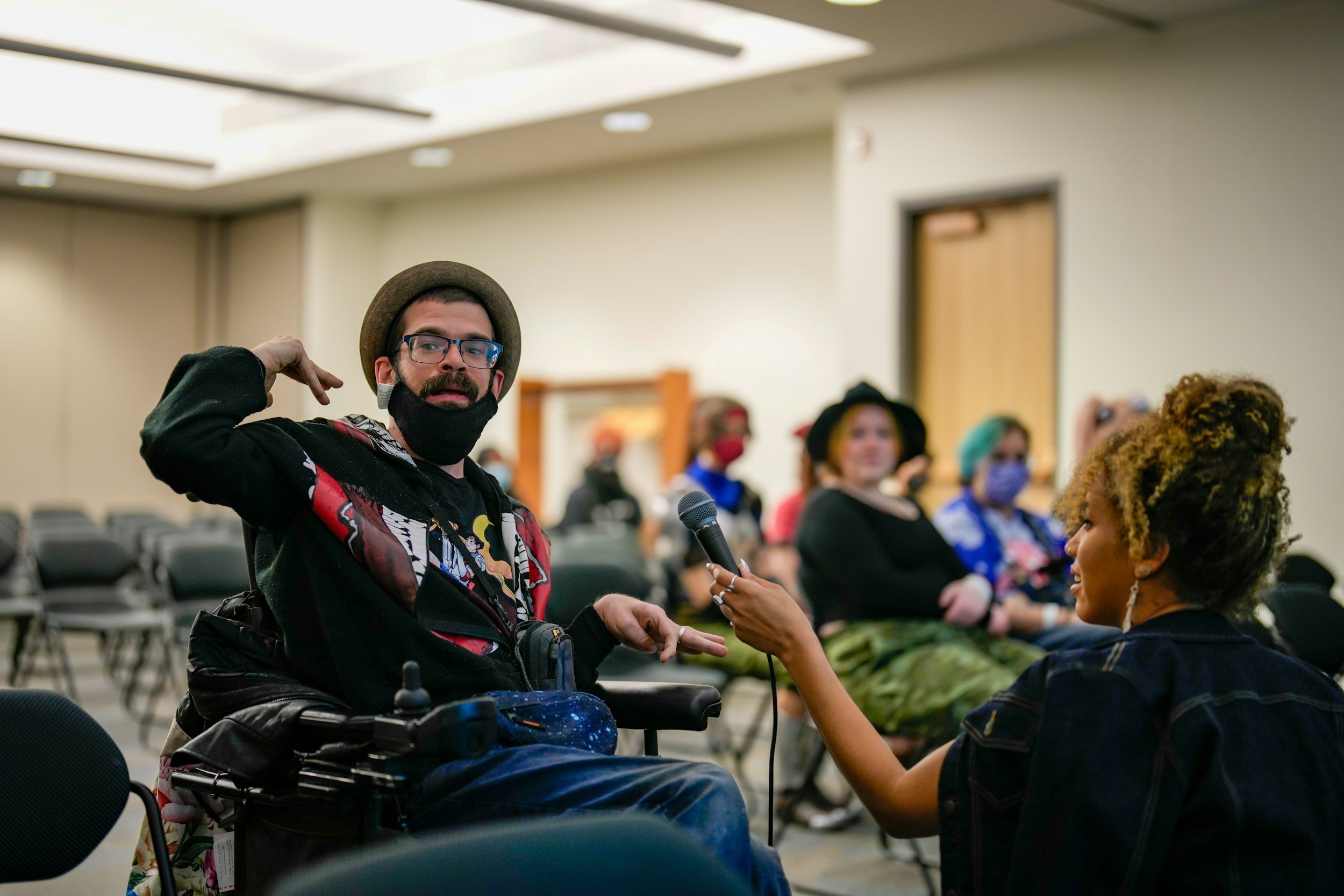 A man in a wheelchair converses with a woman, both displaying friendly expressions and active communication.