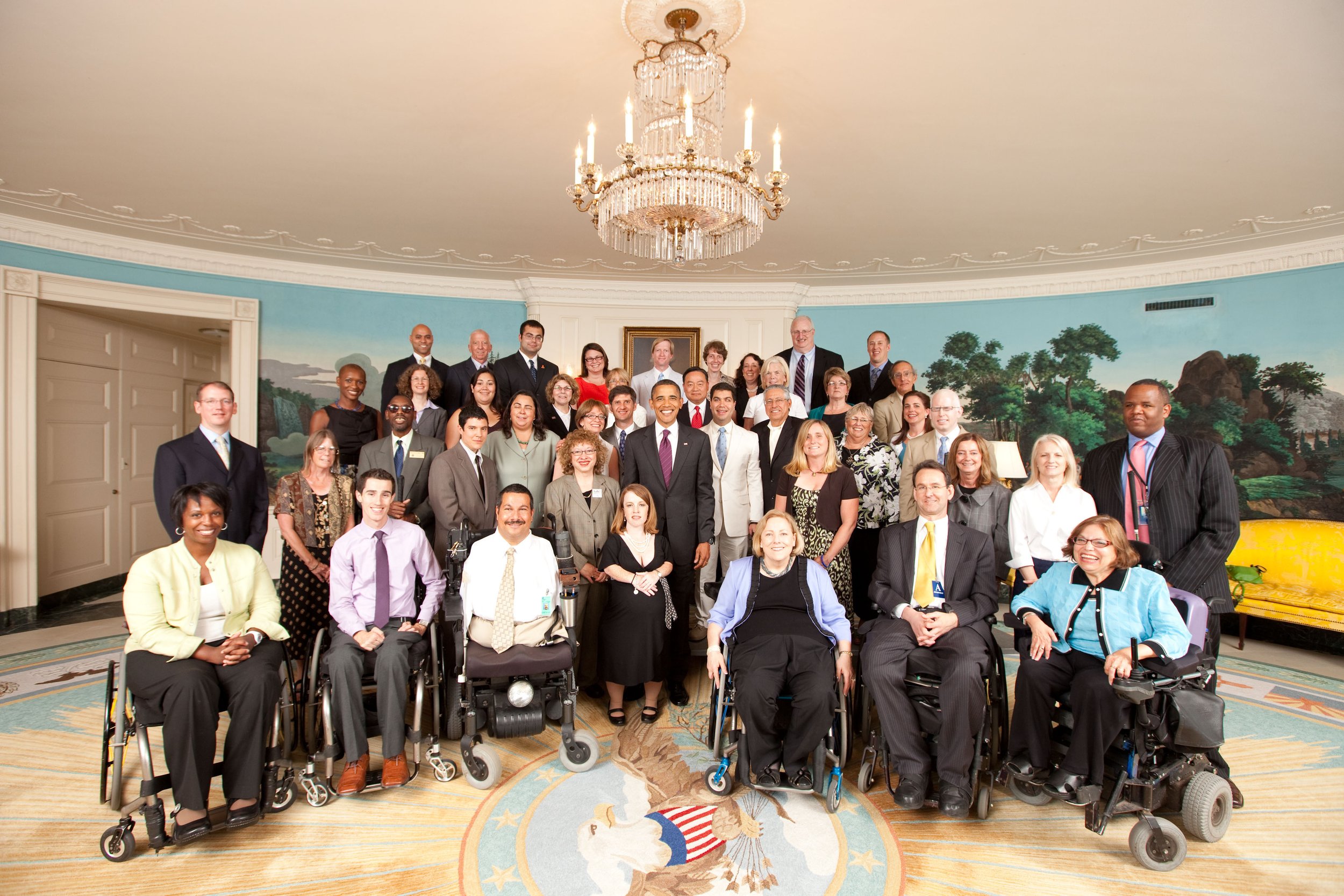 A group of individuals in wheelchairs smiling and posing together for a photo outdoors.