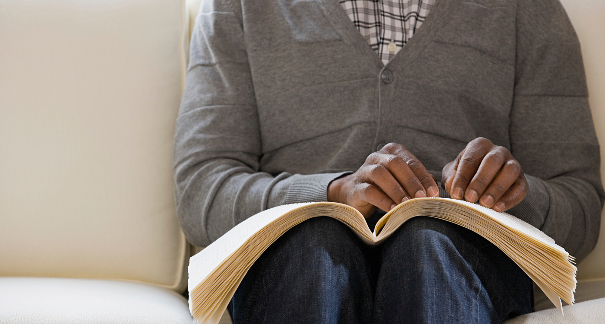A man sitting on a couch, deeply focused on reading a book in a cozy living room setting.