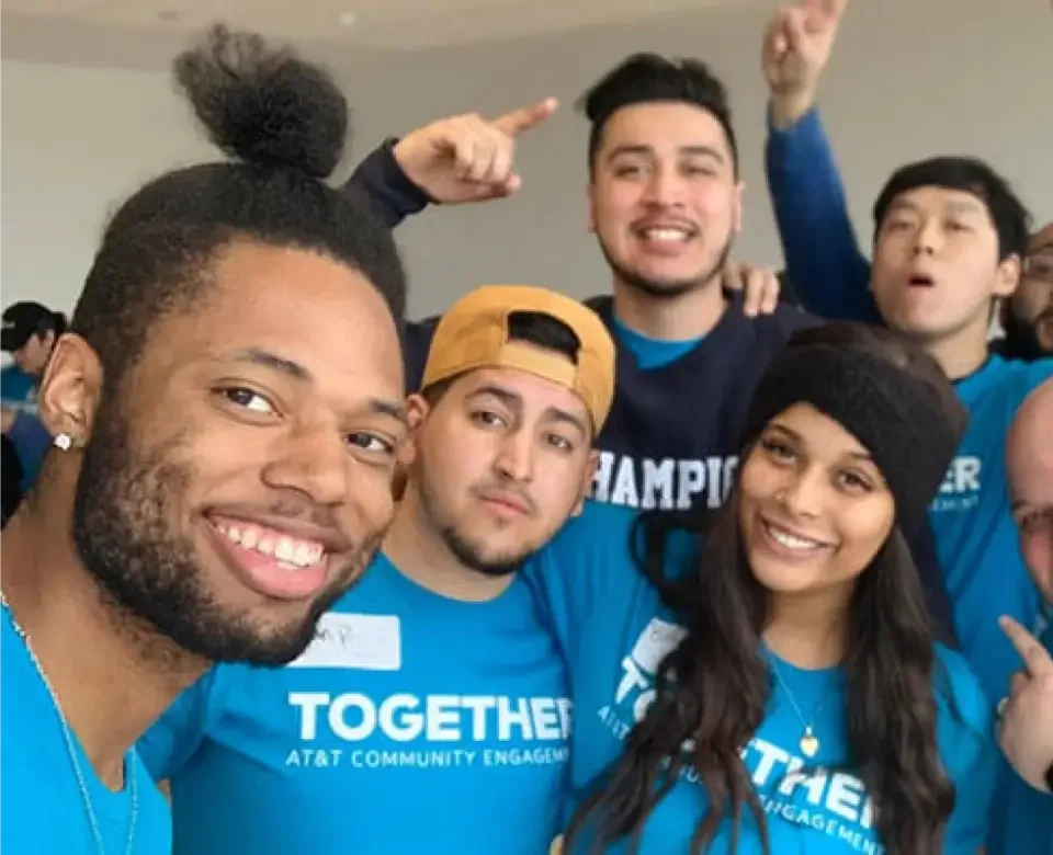 A group of people in blue shirts raising their hands in a display of enthusiasm or celebration.