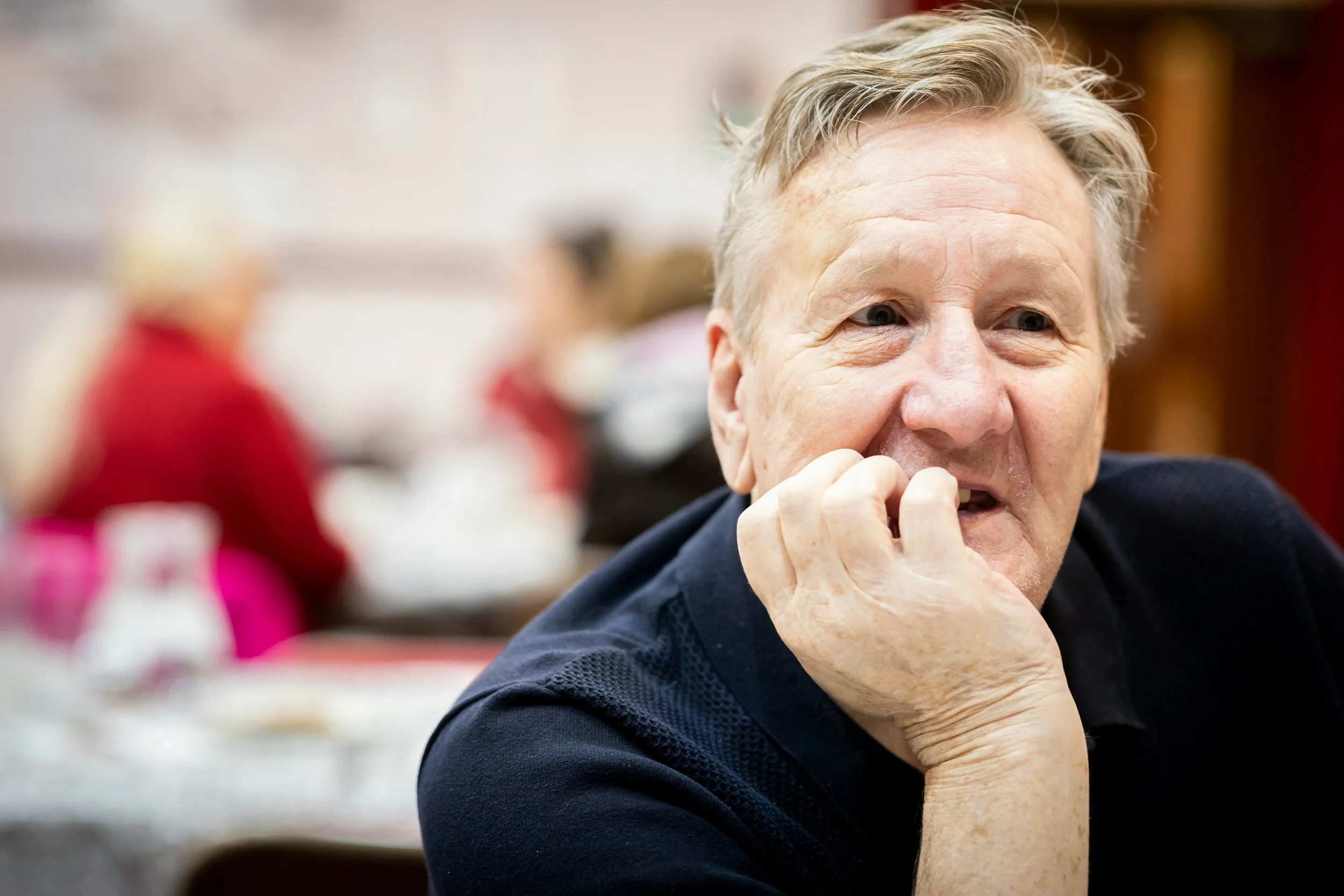 A man sitting at a table, resting his chin on his hand, appears deep in thought.
