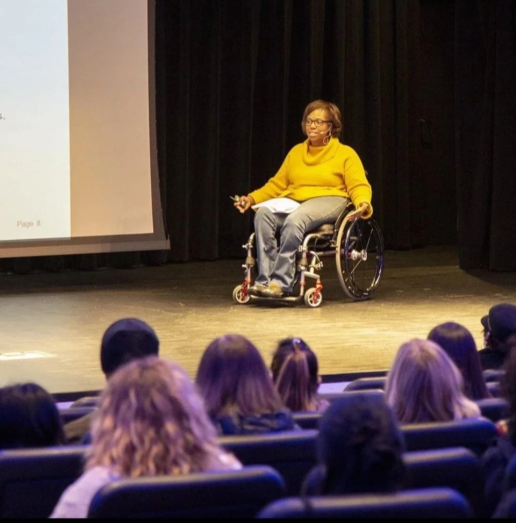 A woman in a wheelchair delivers a speech to an attentive audience, showcasing her message and presence.