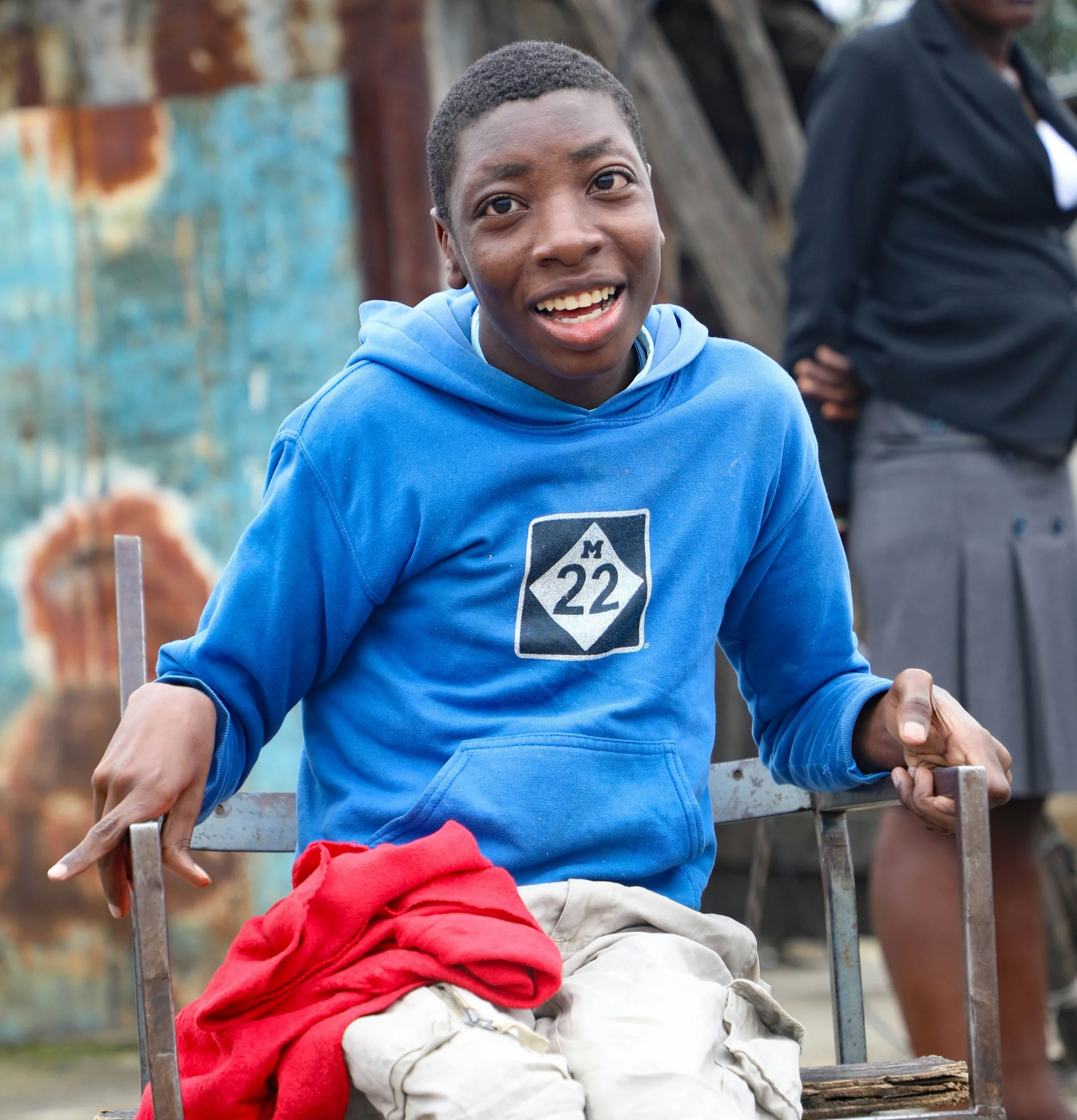 A young man wearing a blue hoodie smiles warmly at the camera.