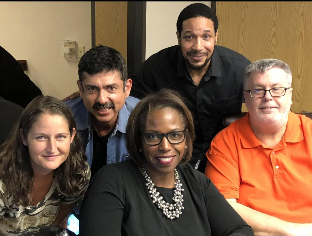 A group of five people smiling and posing together, holding a laptop in front of them for a photo.