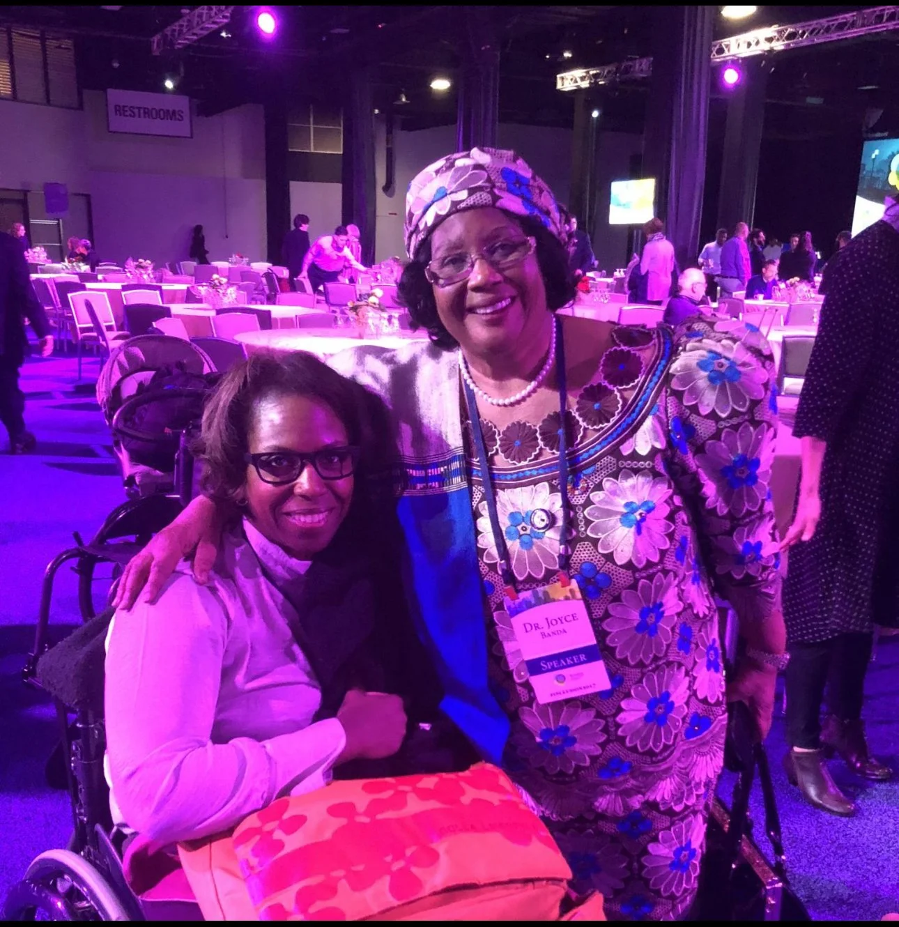 Two women smiling at the camera, enjoying their time together at a lively event.