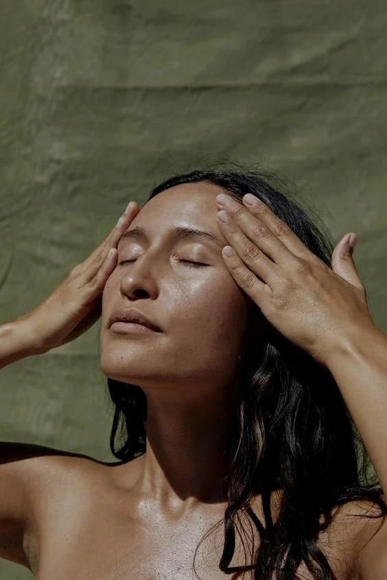 Woman with dark hair applying skincare or massage, with her eyes closed and hands on her forehead.