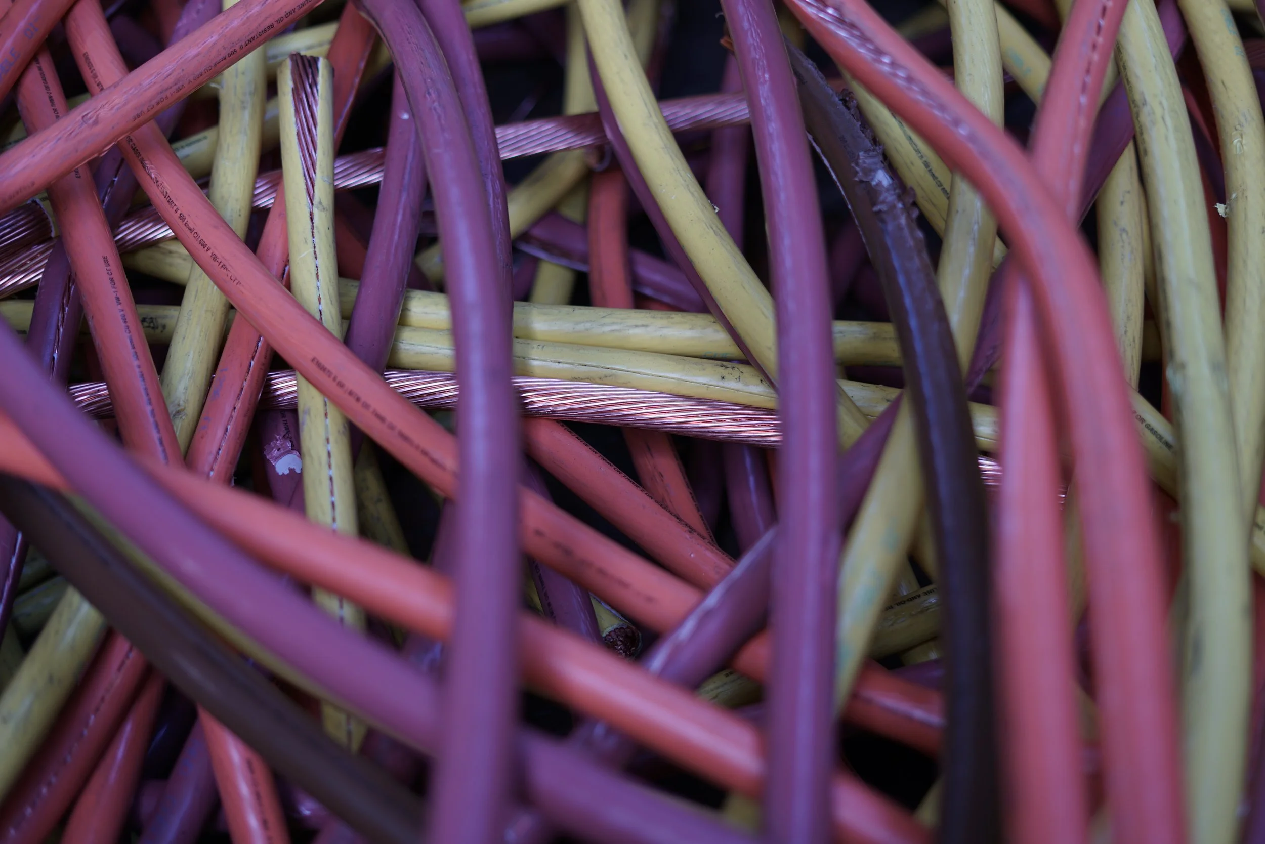 A close-up image of tangled colorful wires in shades of pink, yellow, purple, and beige.
