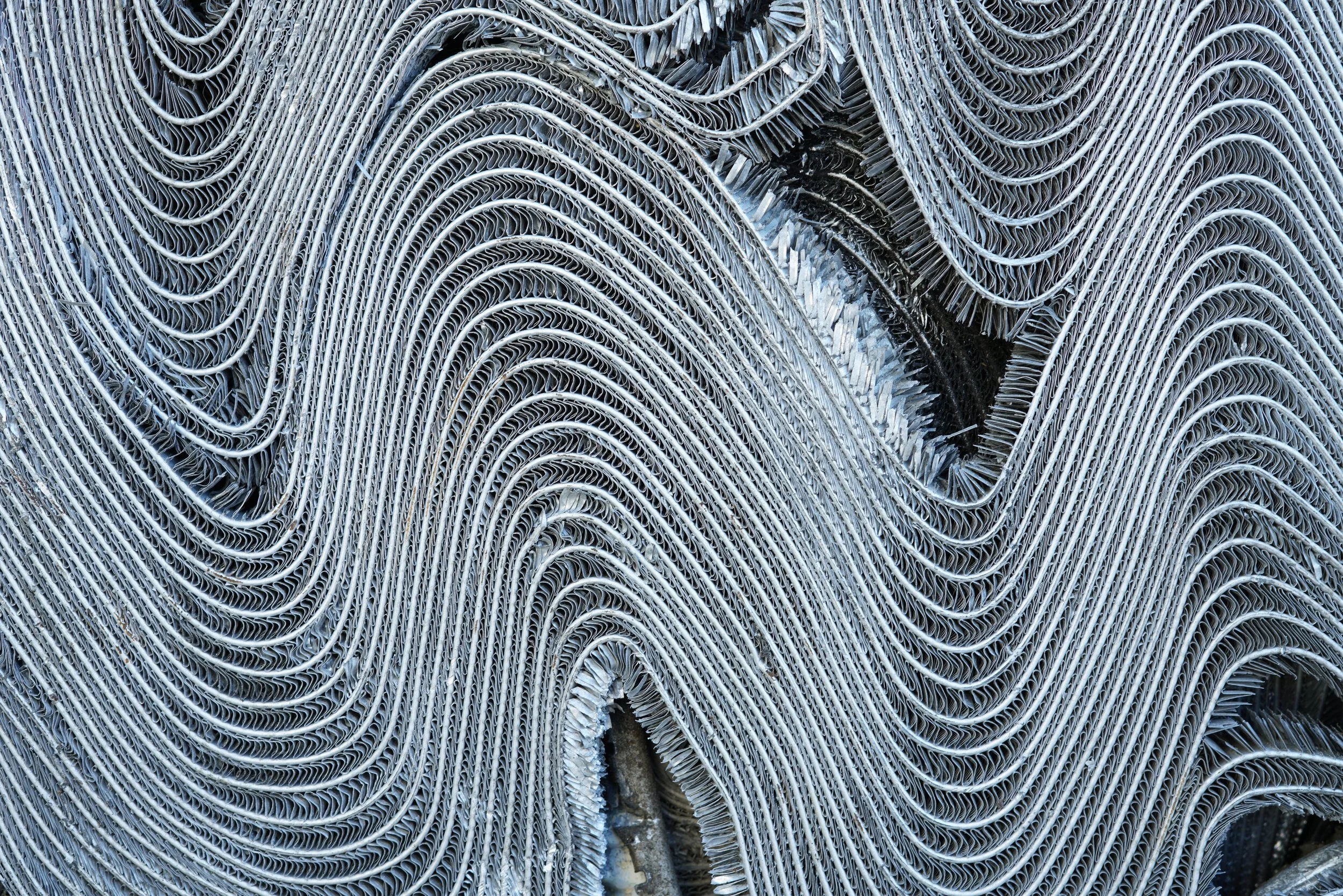 Close-up of an intricate, layered metallic sculpture with flowing, curved patterns and sharp edges.