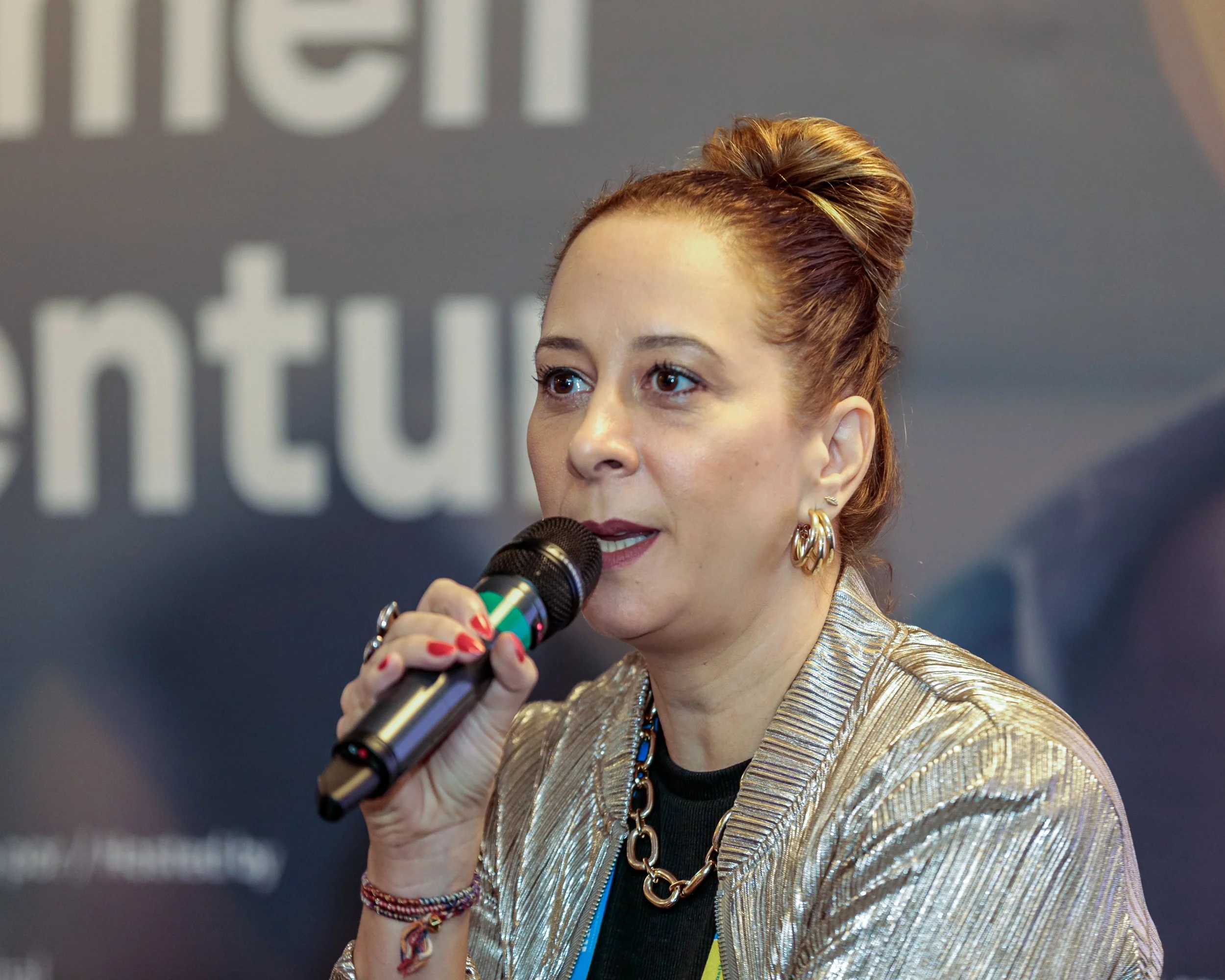 Woman with red hair in a bun speaking into a microphone at an event.