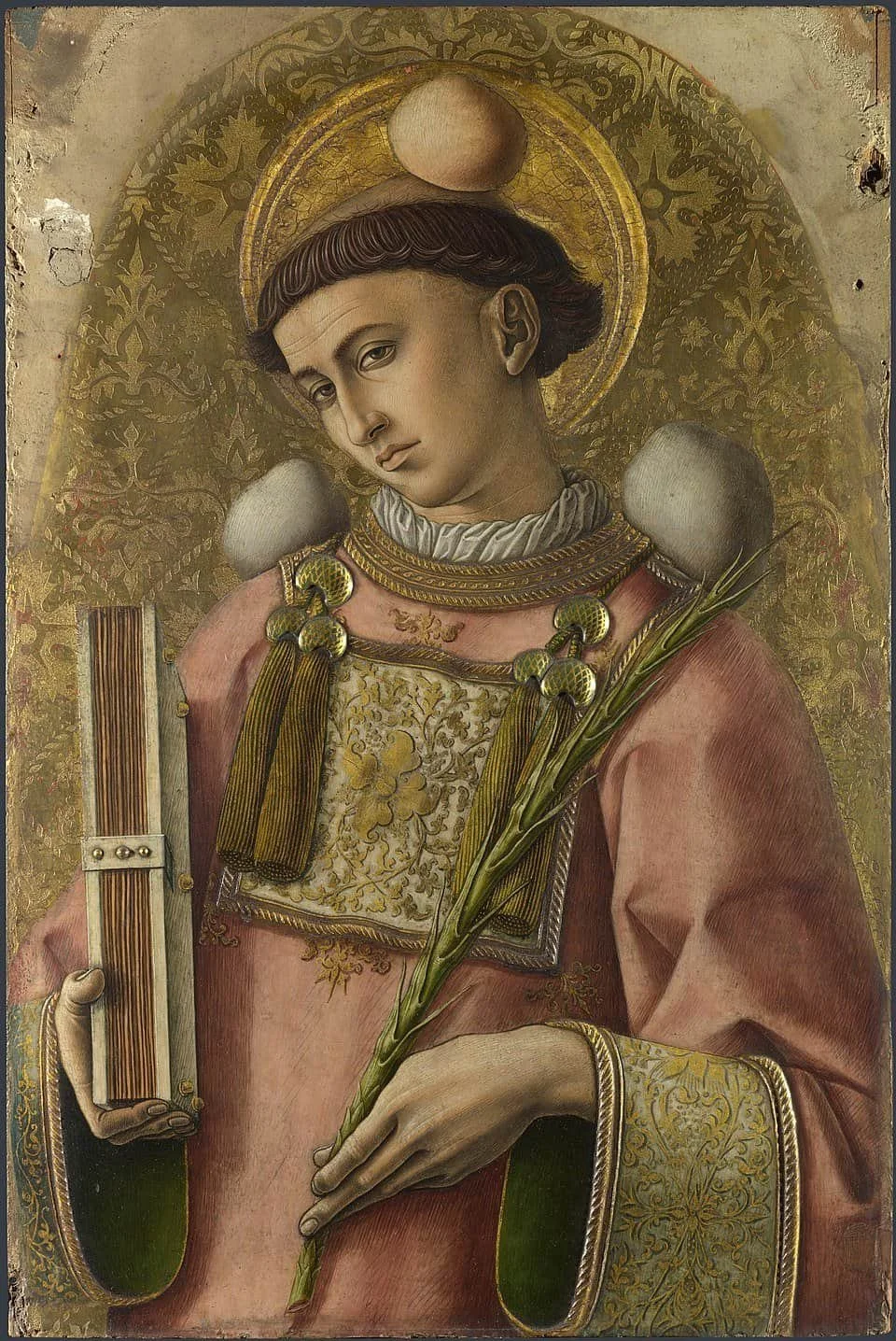 Close up on the Saint Stephen panel in The Demidoff Altarpiece, painted by Carlo Crivelli, egg tempera on wood. The saint has a tonsure and wears a pink robe. He holds a martyr's palm in one hand and a book of the Gospels in the other.