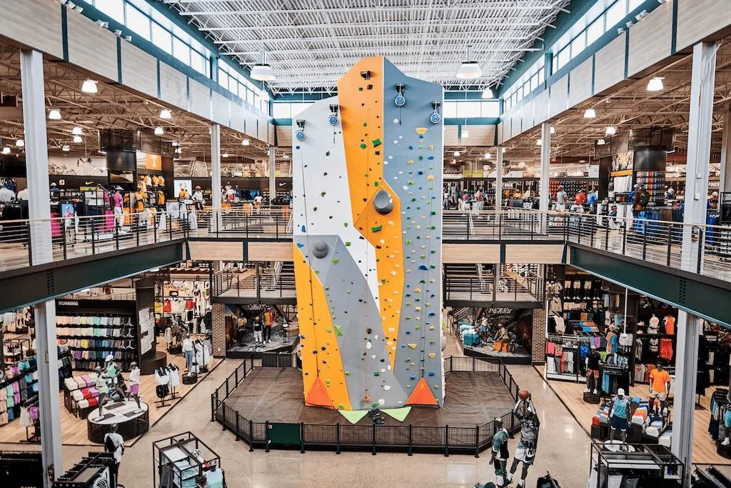Photograph of the interior of Dick's Sporting Goods House of Sport in Knoxville, TN. There is a large, two-story climbing wall in the middle of the store that can accomodate five climbers at once. There are also places to test gear in real conditions