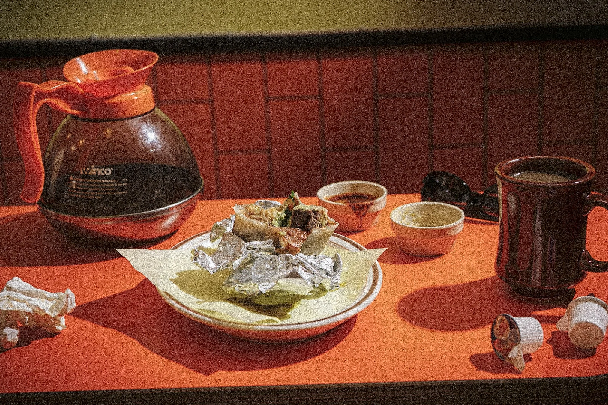 Diner table with a glass coffee carafe, burrito on a plate, dipping sauces, and a coffee mug