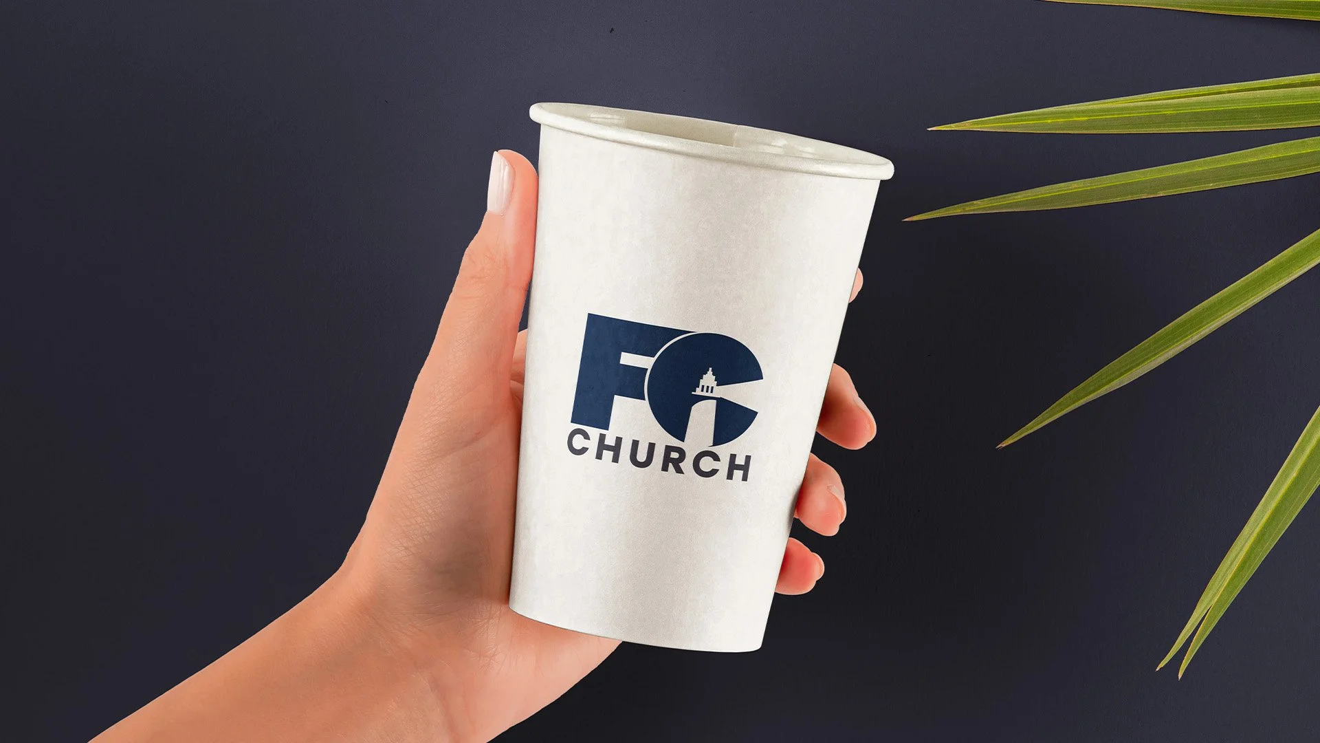 A person holding a white cup with a church logo and the words 'FO Church' against a dark background with green leaves.