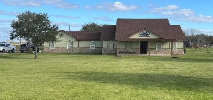 A large single-story house with a brick and beige exterior, a gable roof, and a lawn in front.